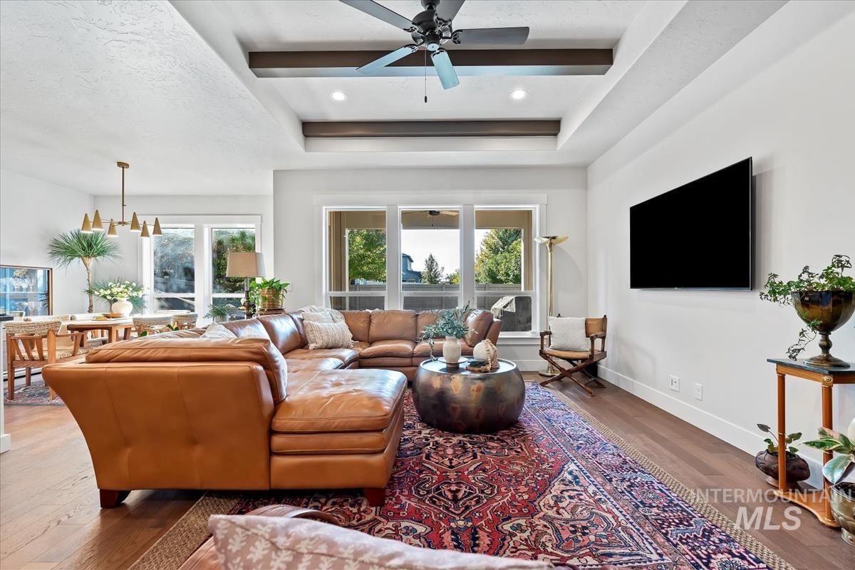 Living area with a raised ceiling, wood finished floors, ceiling fan, a chandelier, and recessed lighting