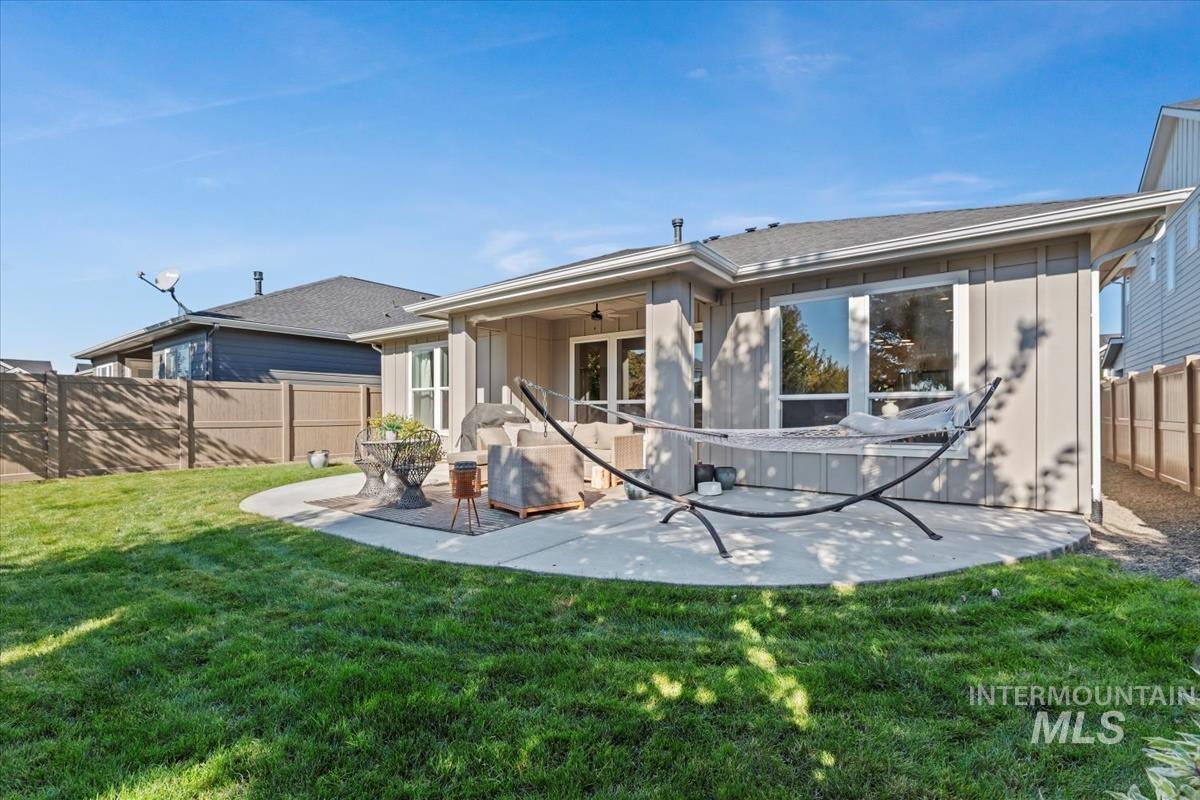 Back of property with a fenced backyard, a ceiling fan, board and batten siding, and a patio area