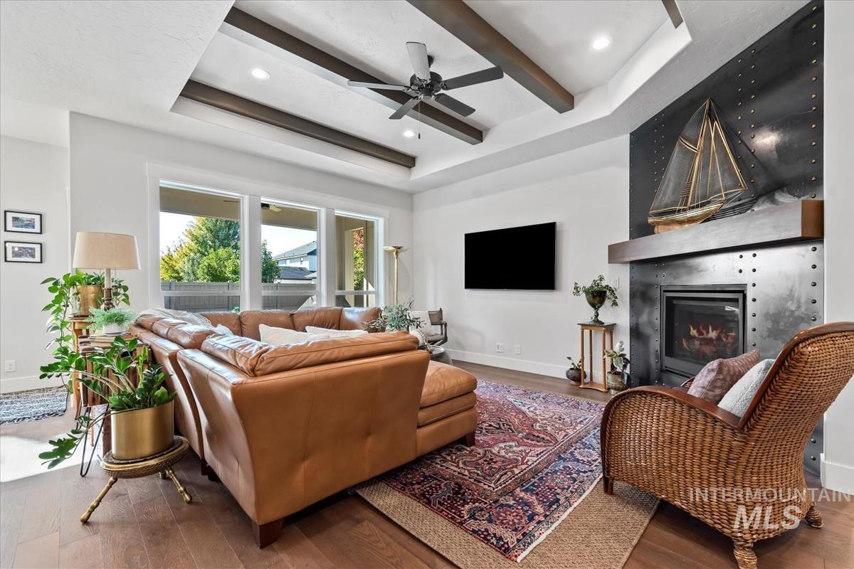 Living area with beamed ceiling, wood finished floors, a fireplace, a tray ceiling, and a ceiling fan