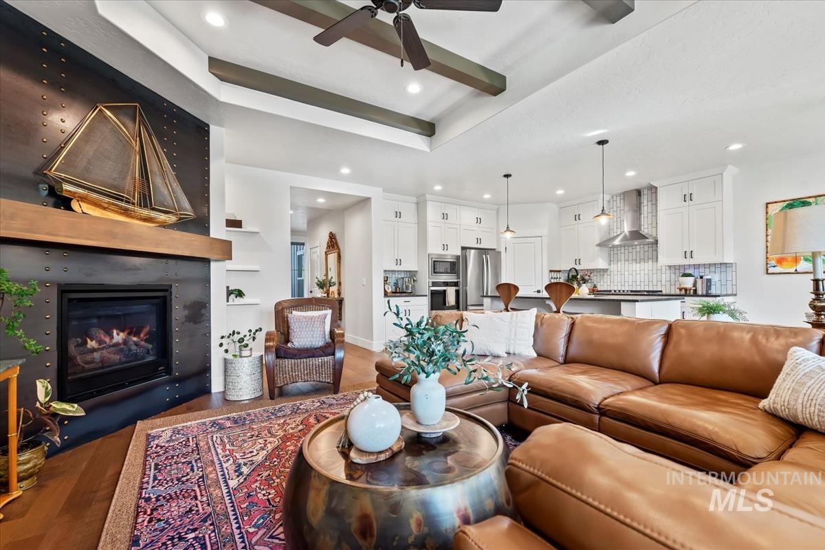 Living area featuring a raised ceiling, wood finished floors, a large fireplace, a ceiling fan, and recessed lighting