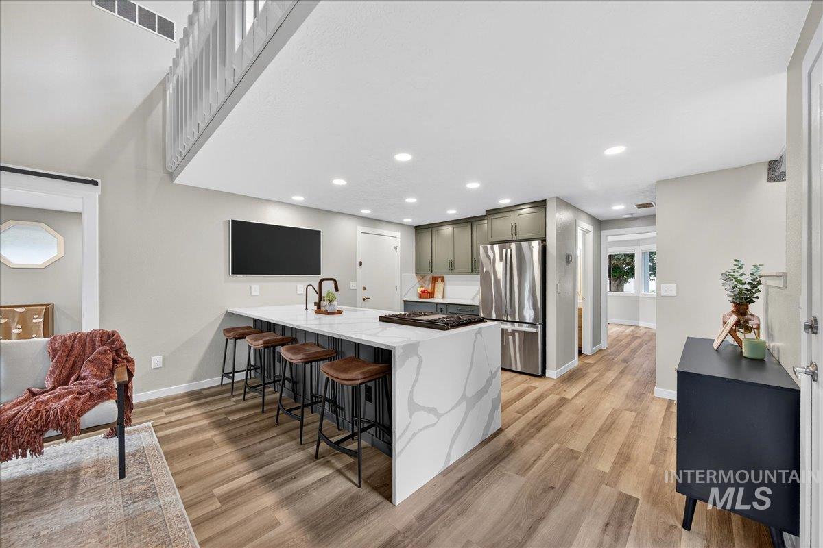 Kitchen featuring a peninsula, a breakfast bar area, light stone counters, appliances with stainless steel finishes, and light wood-style floors