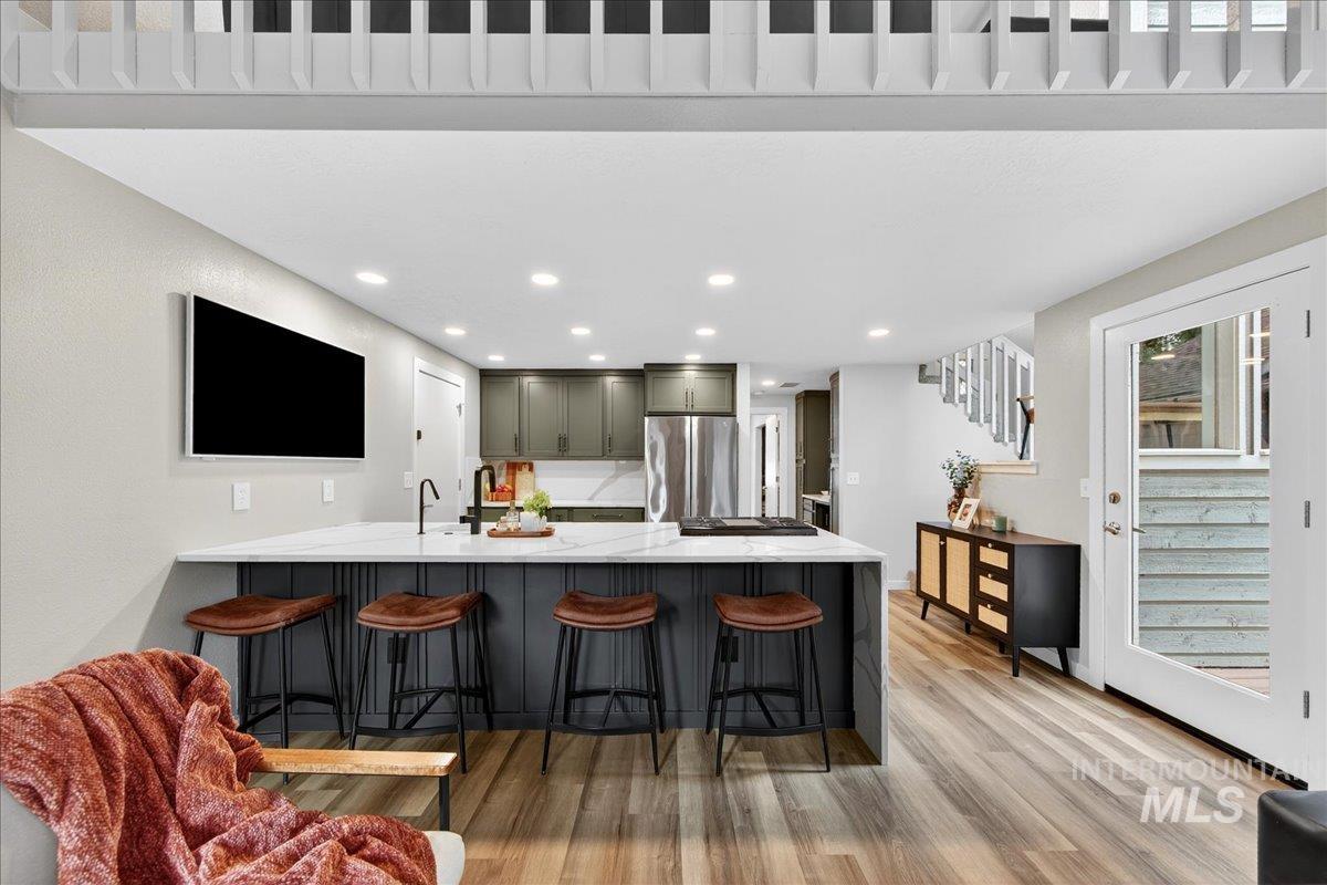 Kitchen with a peninsula, a breakfast bar area, light stone counters, light wood-type flooring, and recessed lighting