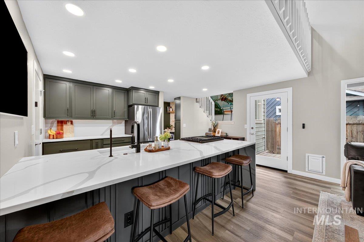 Kitchen with a kitchen breakfast bar, light stone counters, light wood-style flooring, appliances with stainless steel finishes, and gray cabinets