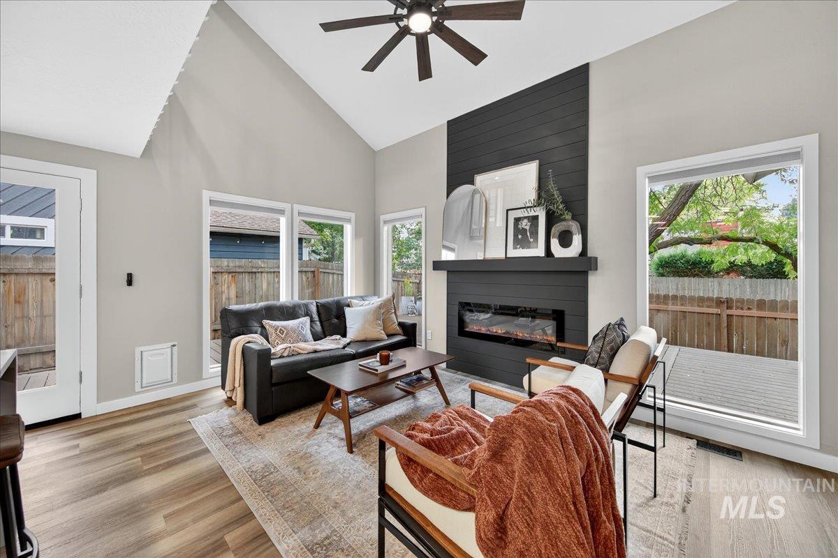 Living area featuring high vaulted ceiling, light wood-style flooring, a large fireplace, and a ceiling fan