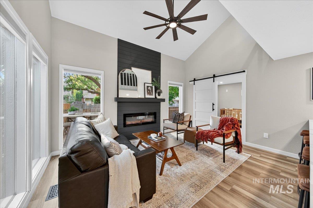 Living room with a barn door, high vaulted ceiling, light wood-style floors, a ceiling fan, and a fireplace