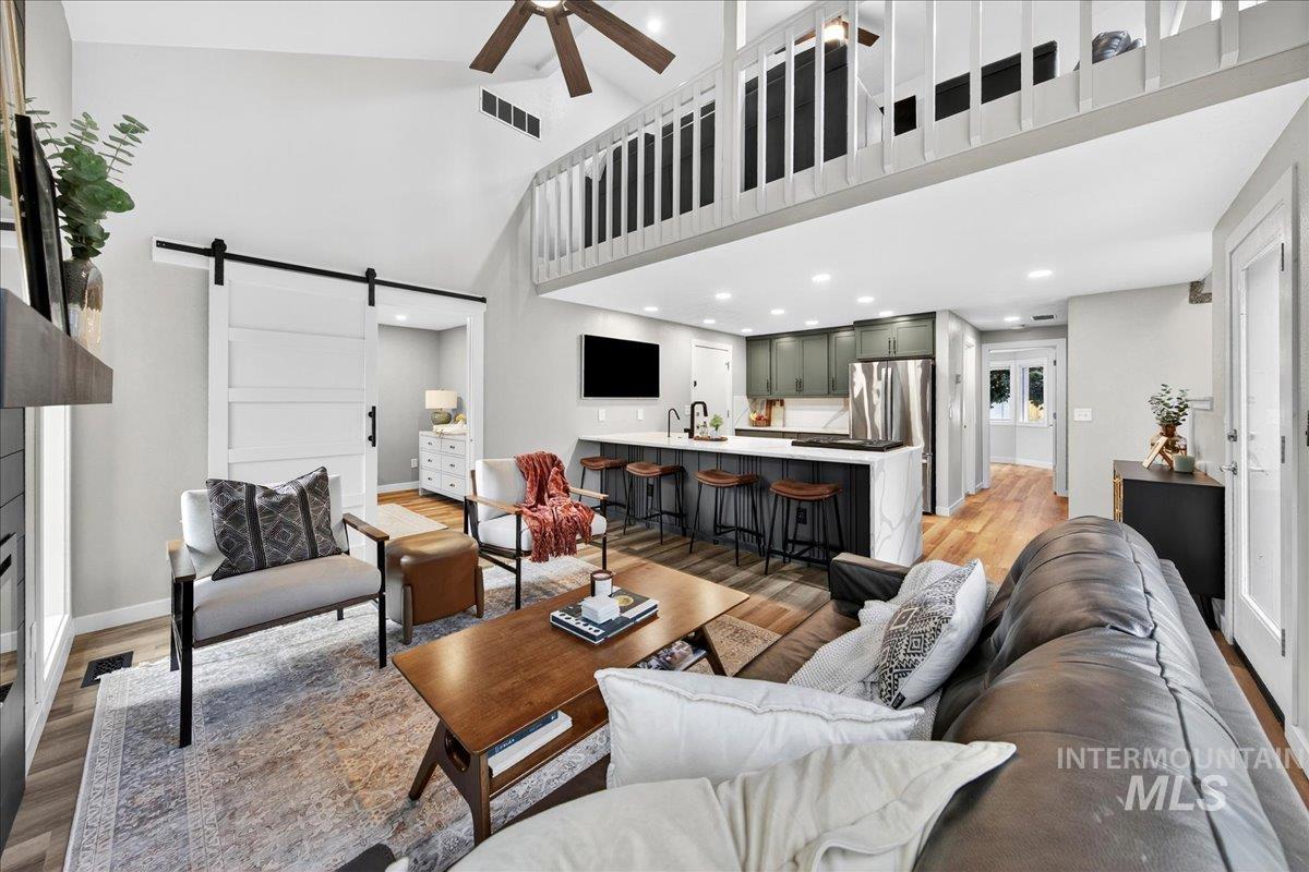 Living area with a barn door, light wood-type flooring, high vaulted ceiling, ceiling fan, and recessed lighting
