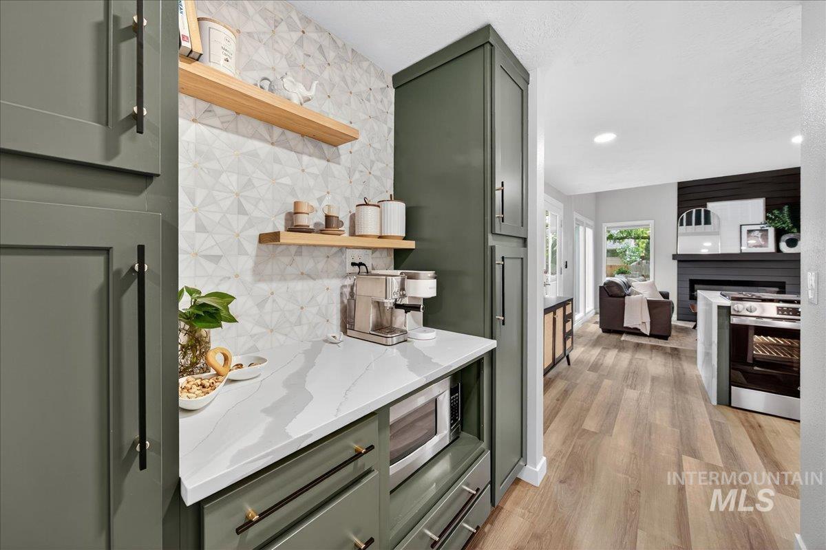 Kitchen featuring green cabinetry, open shelves, decorative backsplash, light stone countertops, and light wood-style flooring