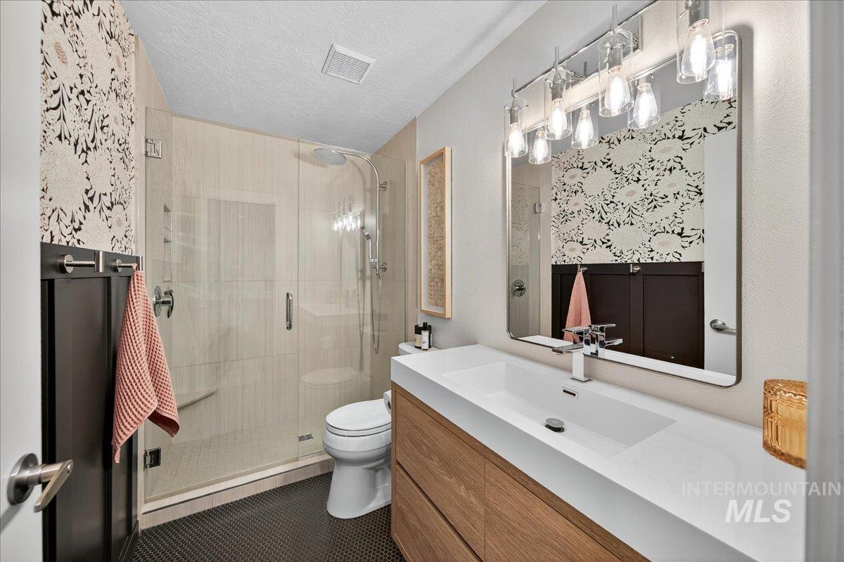 Full bath with a textured ceiling, vanity, a shower stall, and dark tile patterned floors