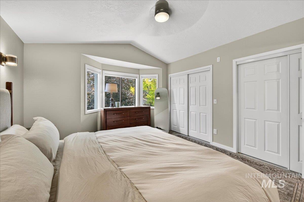 Bedroom featuring vaulted ceiling, two closets, a textured ceiling, and a ceiling fan