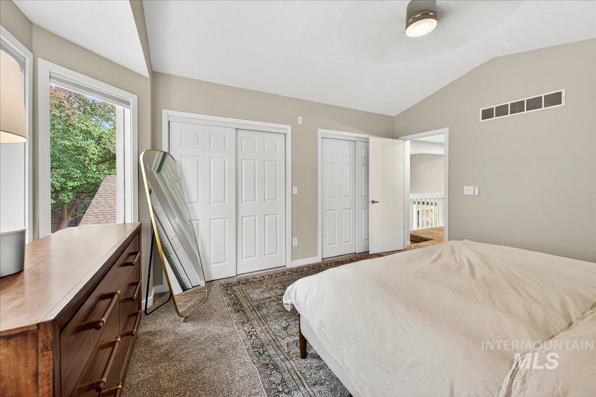 Bedroom with lofted ceiling, two closets, dark colored carpet, and ceiling fan
