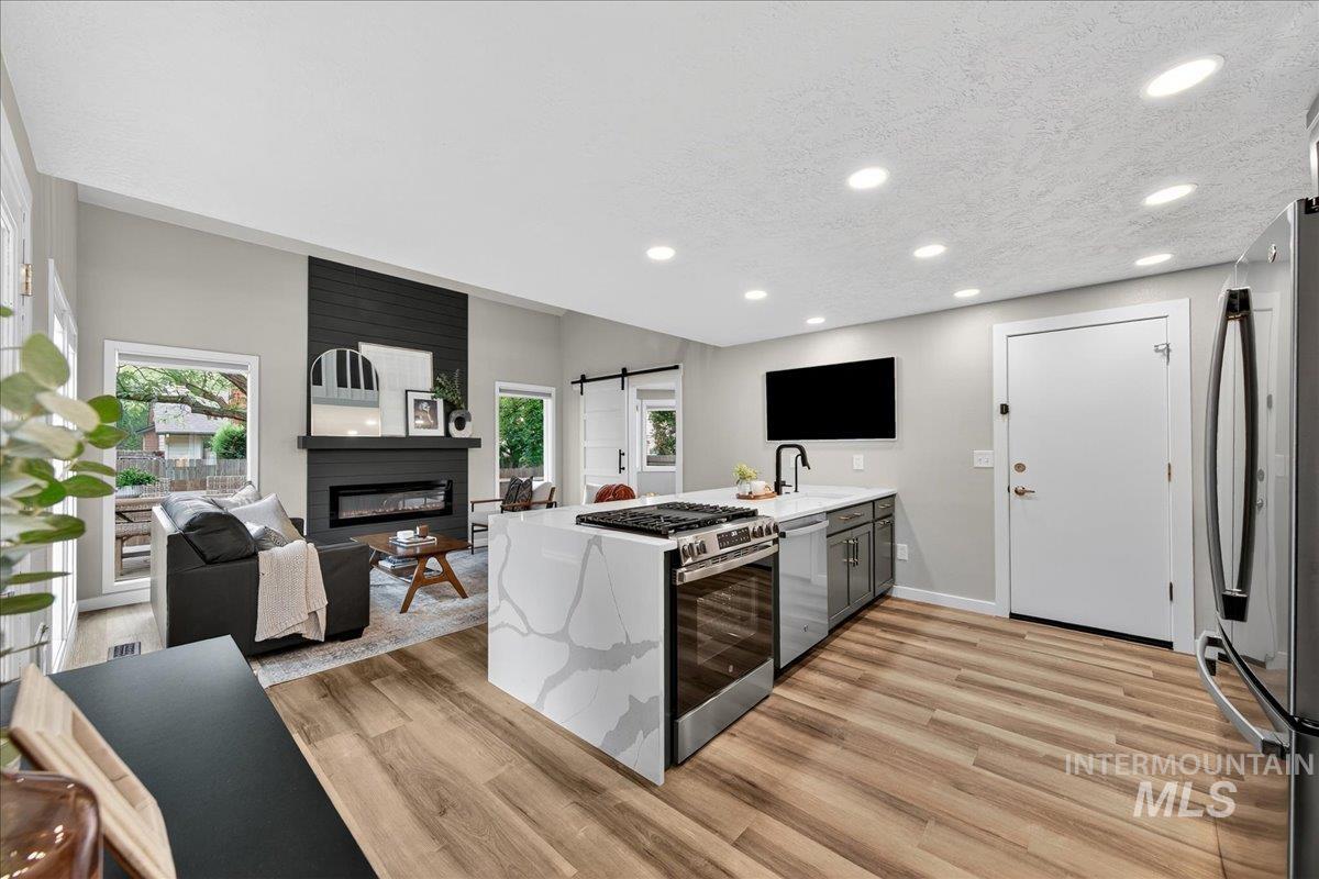 Kitchen with a barn door, a peninsula, stainless steel appliances, a textured ceiling, and light stone counters