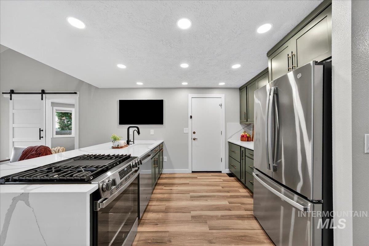 Kitchen with a peninsula, stainless steel appliances, light stone counters, recessed lighting, and a barn door