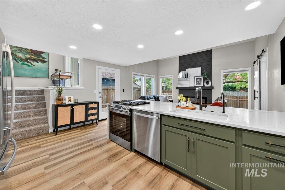 Kitchen featuring green cabinetry, a barn door, appliances with stainless steel finishes, light stone countertops, and light wood-type flooring