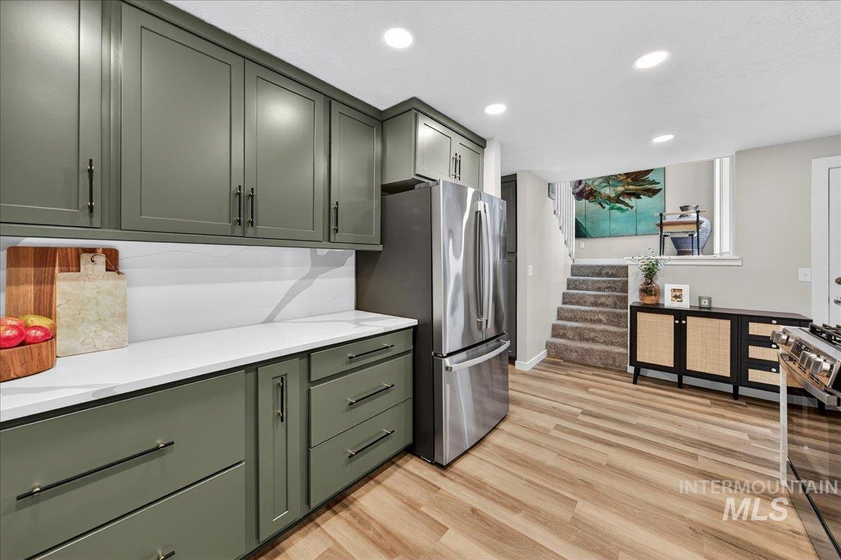 Kitchen with green cabinets, light wood-style flooring, black range with gas cooktop, recessed lighting, and light stone counters