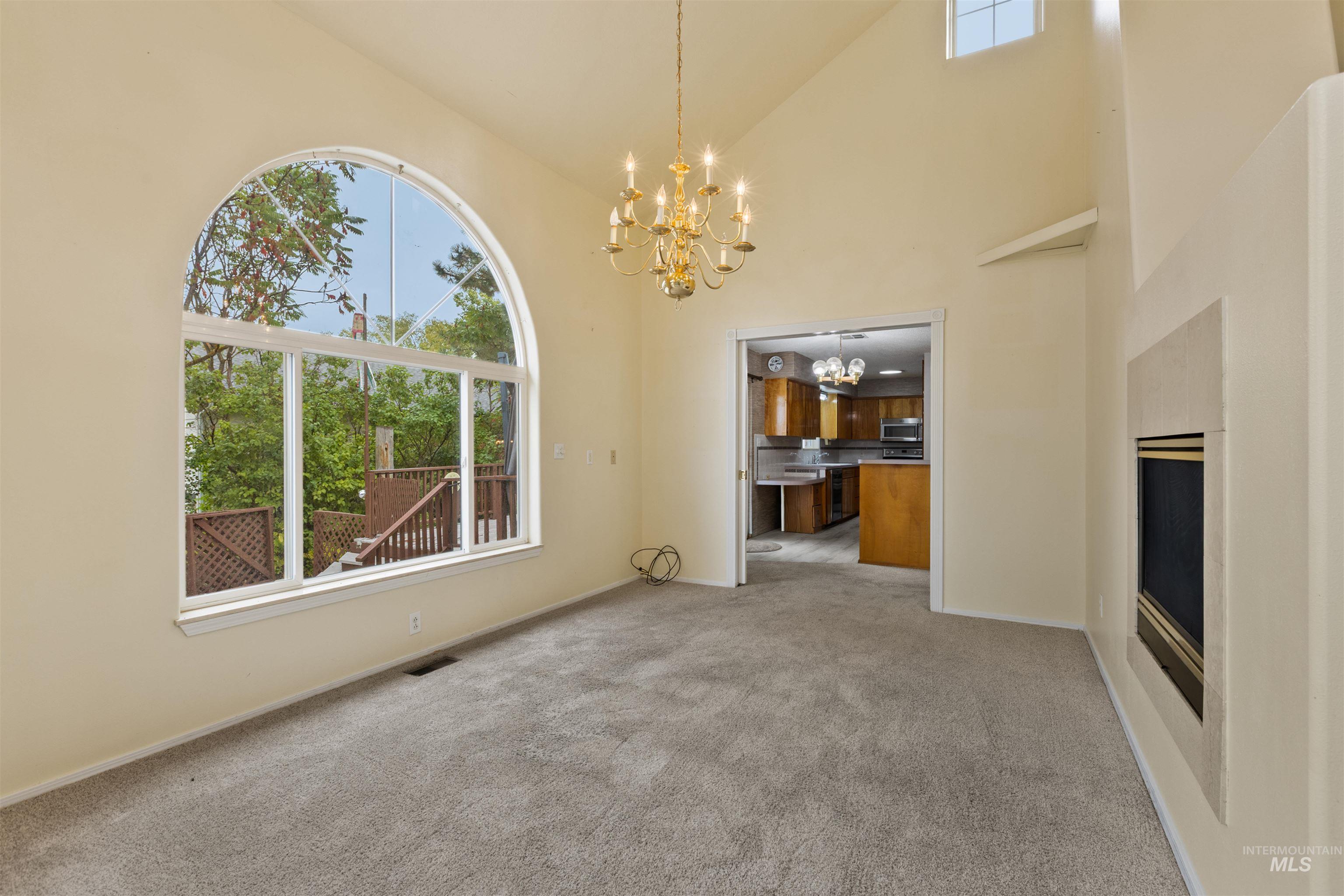 Unfurnished living room featuring carpet, high vaulted ceiling, and a chandelier