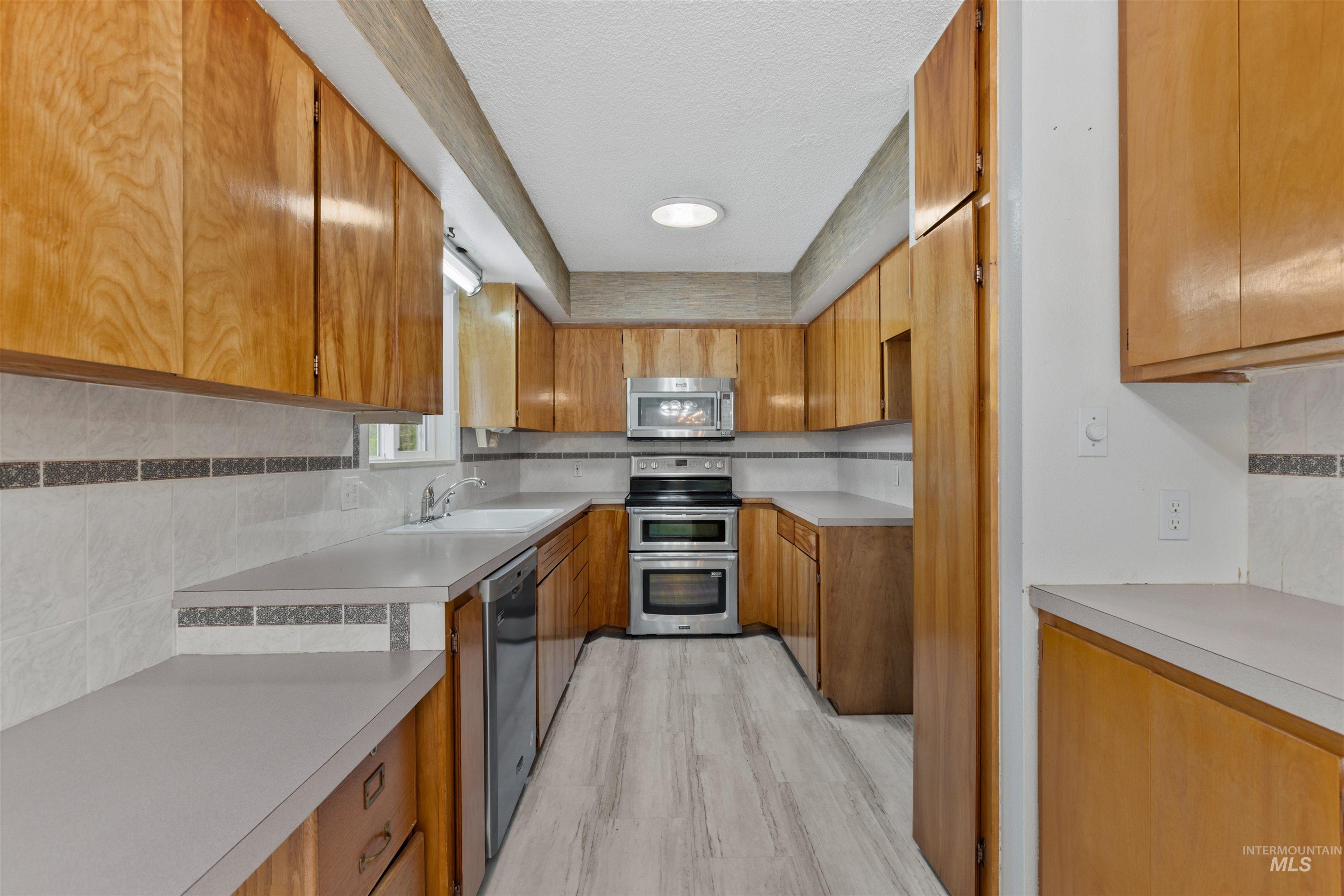 Kitchen featuring tasteful backsplash, brown cabinets, appliances with stainless steel finishes, light countertops, and light wood-type flooring