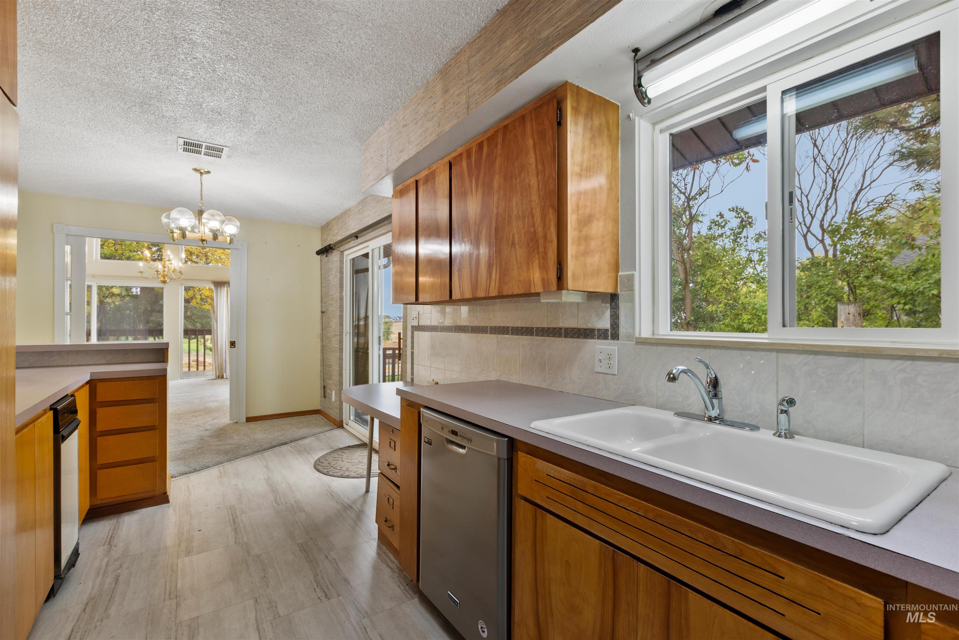 Kitchen featuring brown cabinetry, dishwasher, decorative light fixtures, decorative backsplash, and a textured ceiling