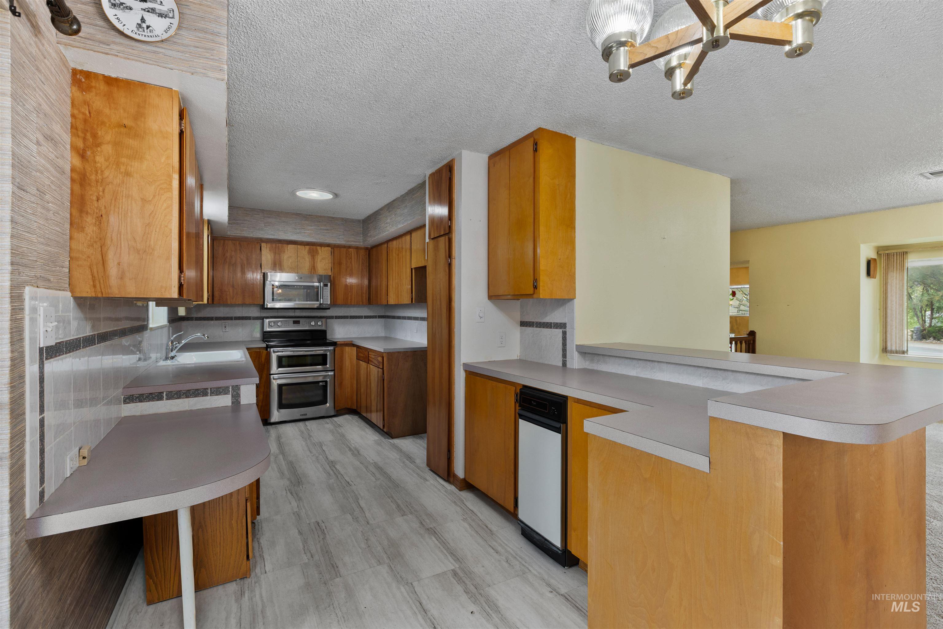 Kitchen with brown cabinetry, a textured ceiling, light countertops, appliances with stainless steel finishes, and a peninsula