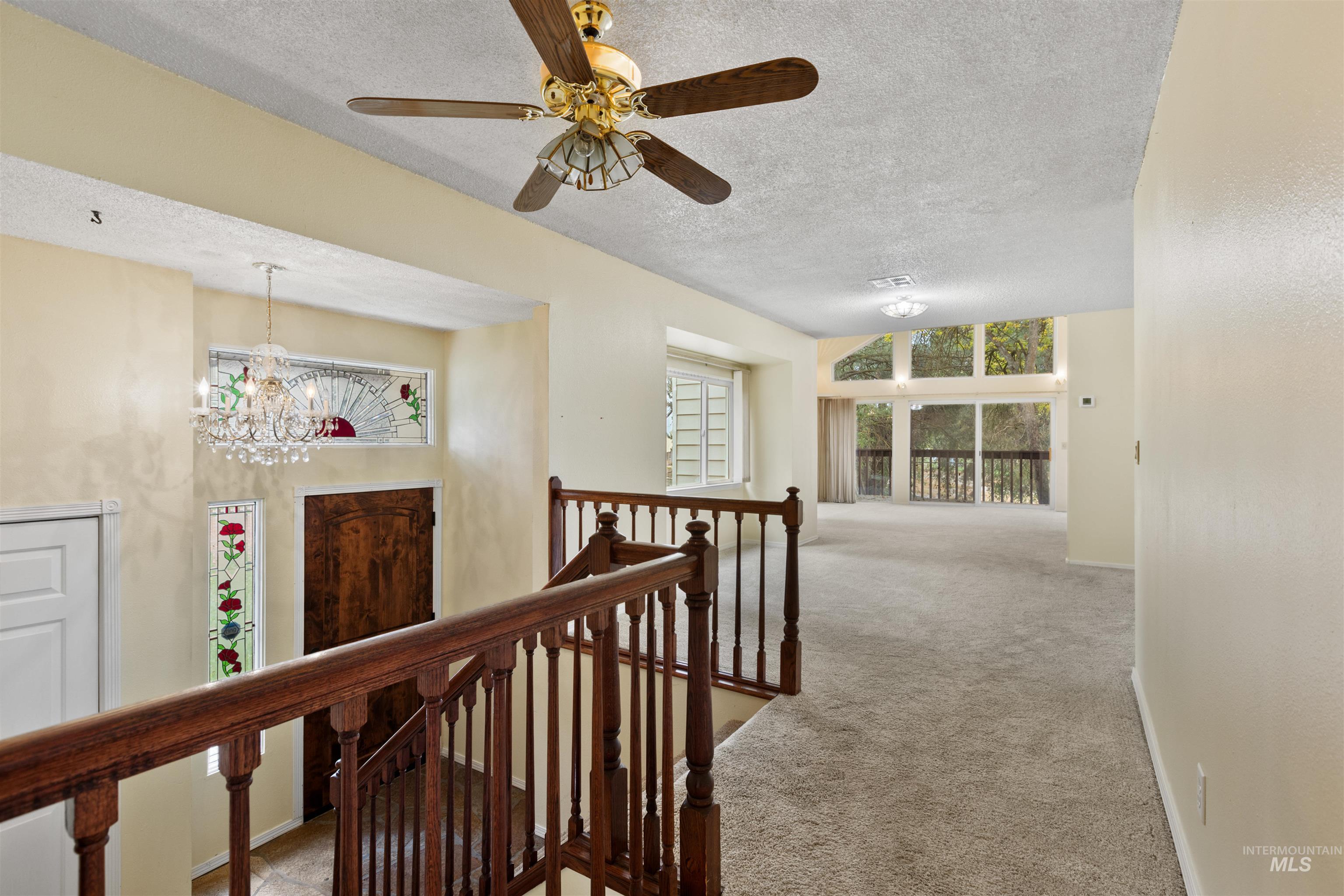 Hall with carpet, an upstairs landing, a textured ceiling, and a chandelier