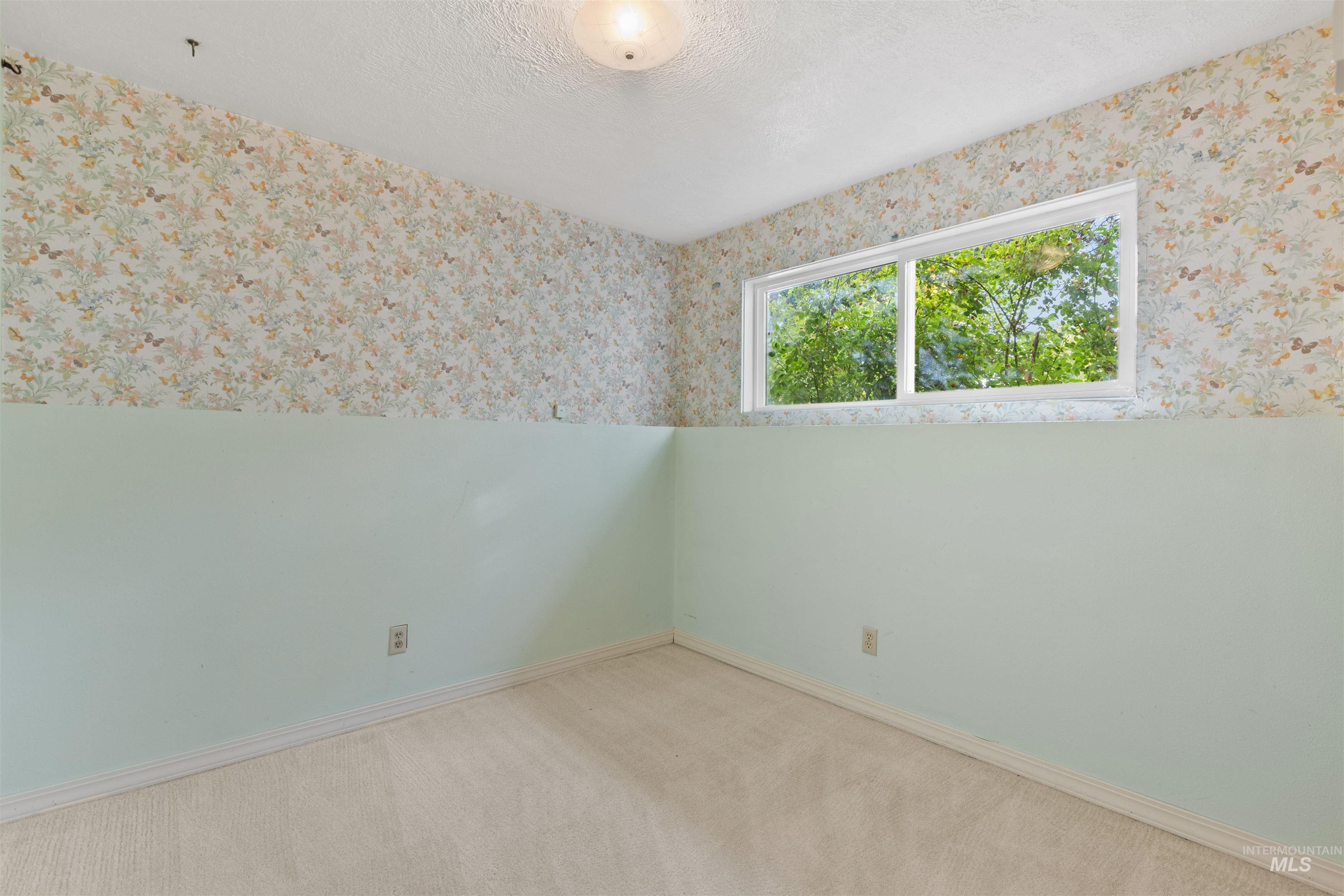 Carpeted spare room featuring a textured ceiling and wallpapered walls