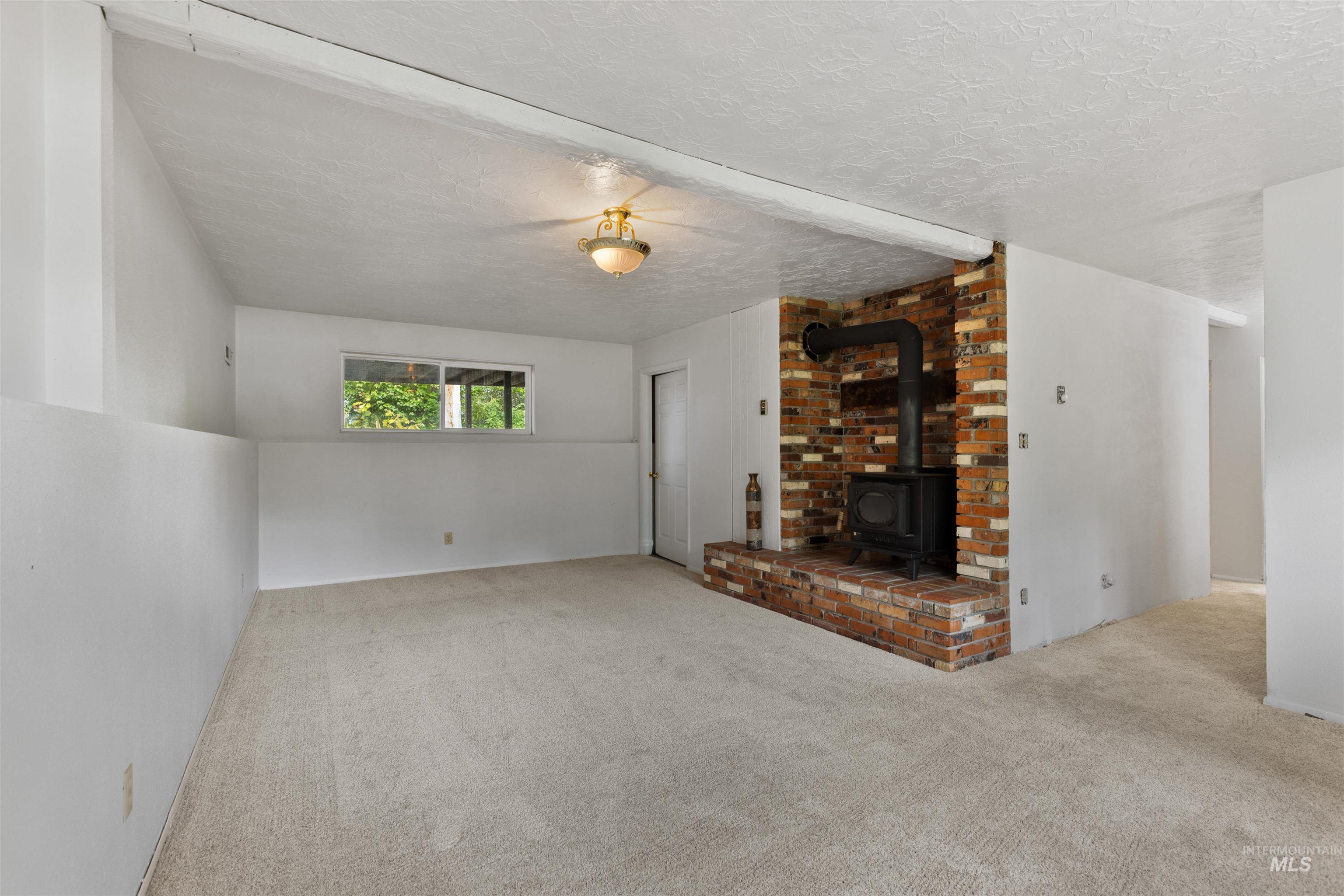 Unfurnished living room with a wood stove, carpet floors, and a textured ceiling