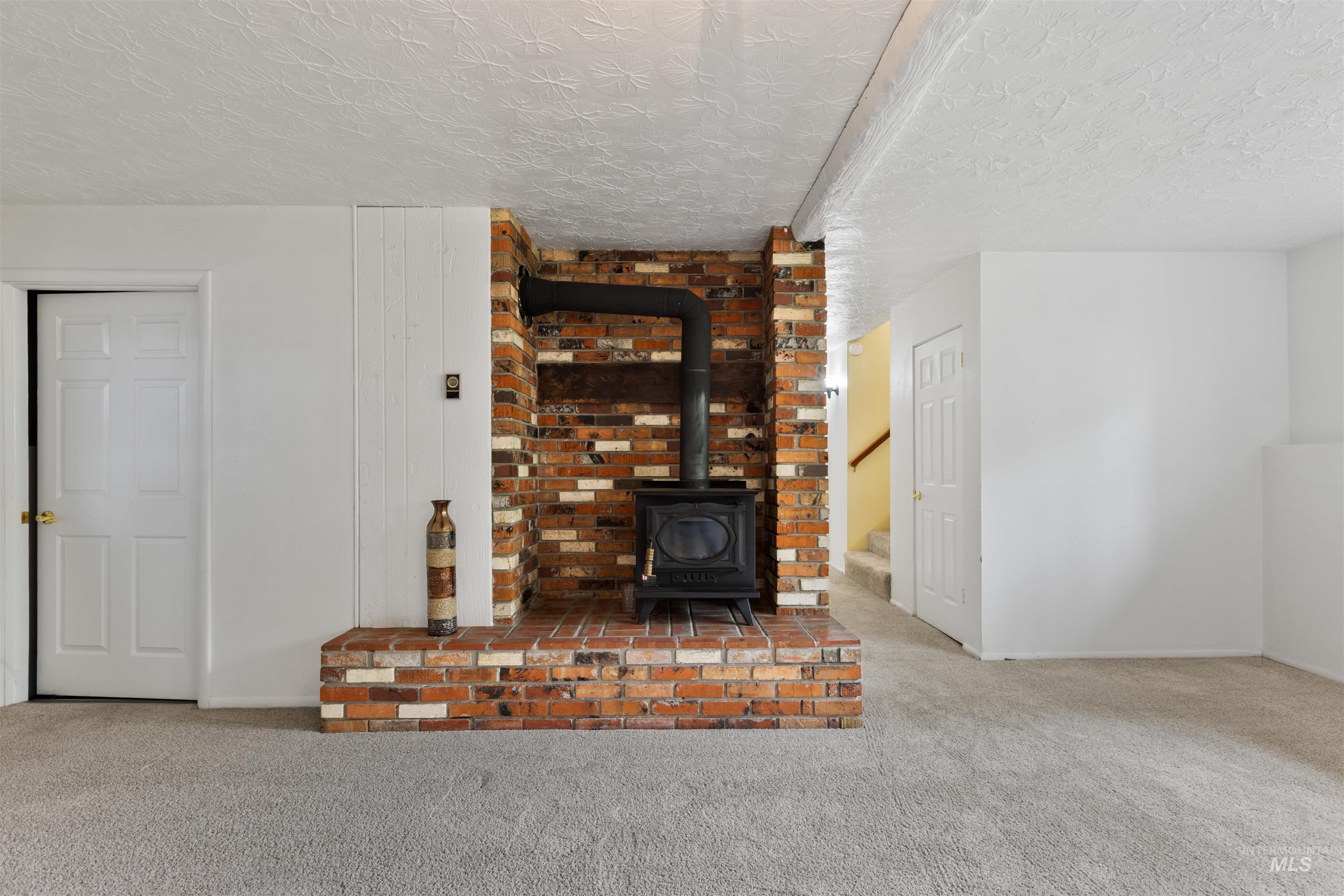Unfurnished living room with a wood stove, carpet flooring, stairs, and a textured ceiling