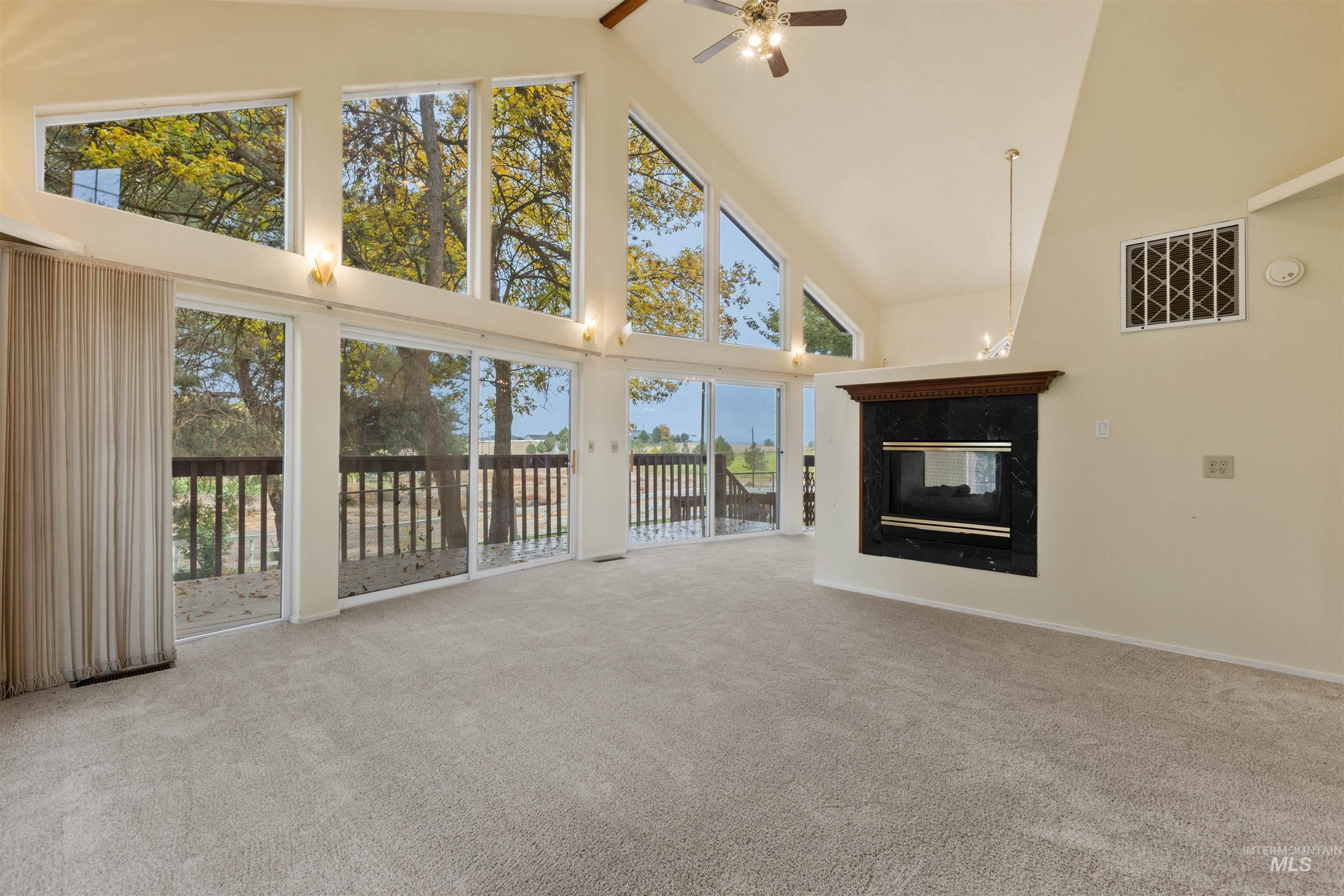 Unfurnished living room with high vaulted ceiling, a multi sided fireplace, light colored carpet, and ceiling fan