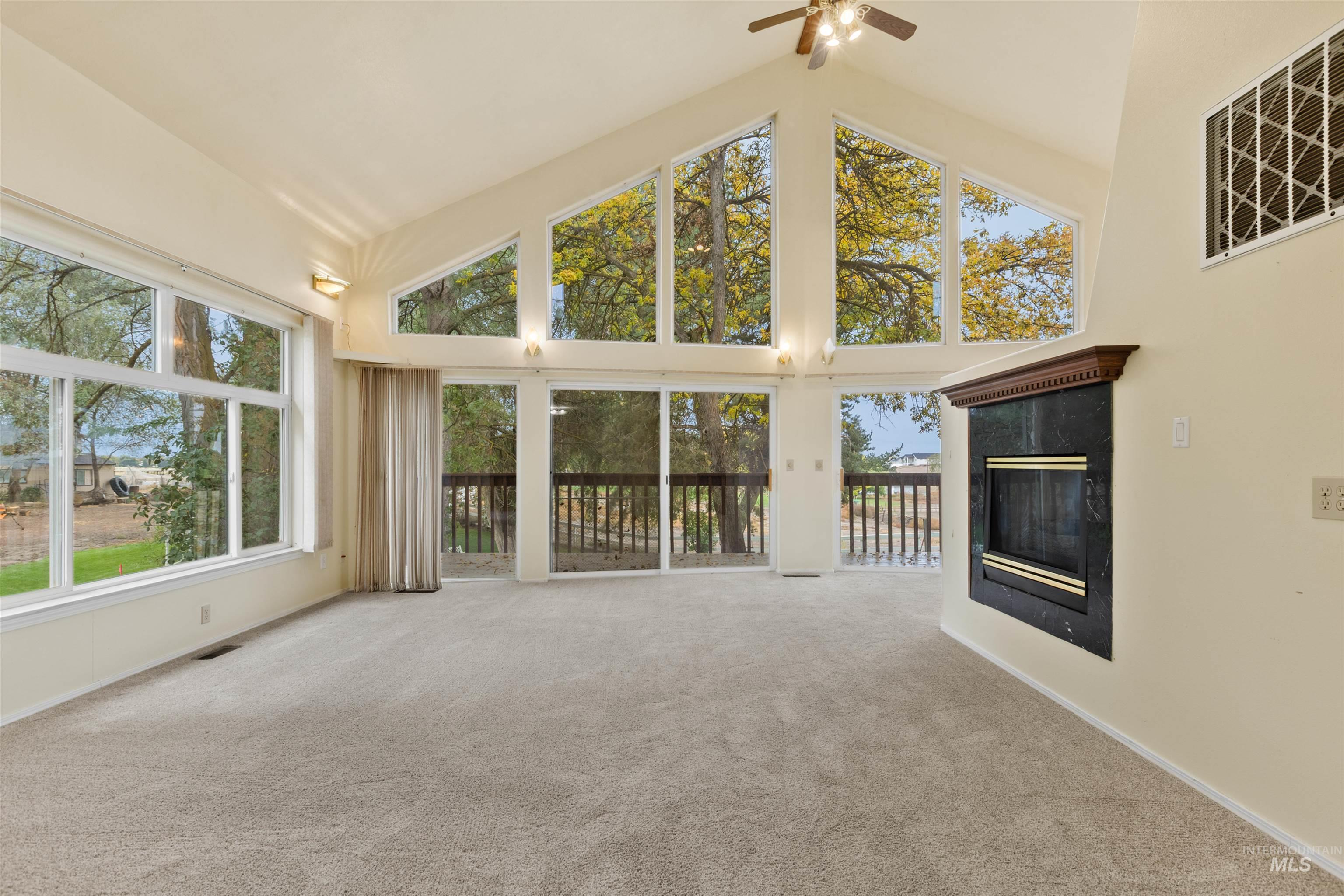 Unfurnished living room featuring high vaulted ceiling, a premium fireplace, plenty of natural light, carpet, and a ceiling fan