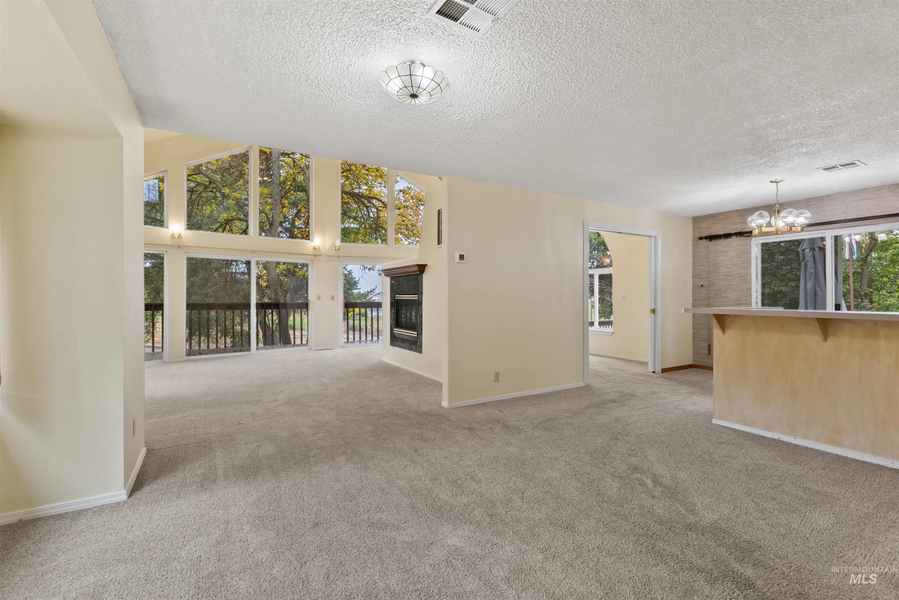 Unfurnished living room with light colored carpet, a chandelier, a glass covered fireplace, a textured ceiling, and a towering ceiling