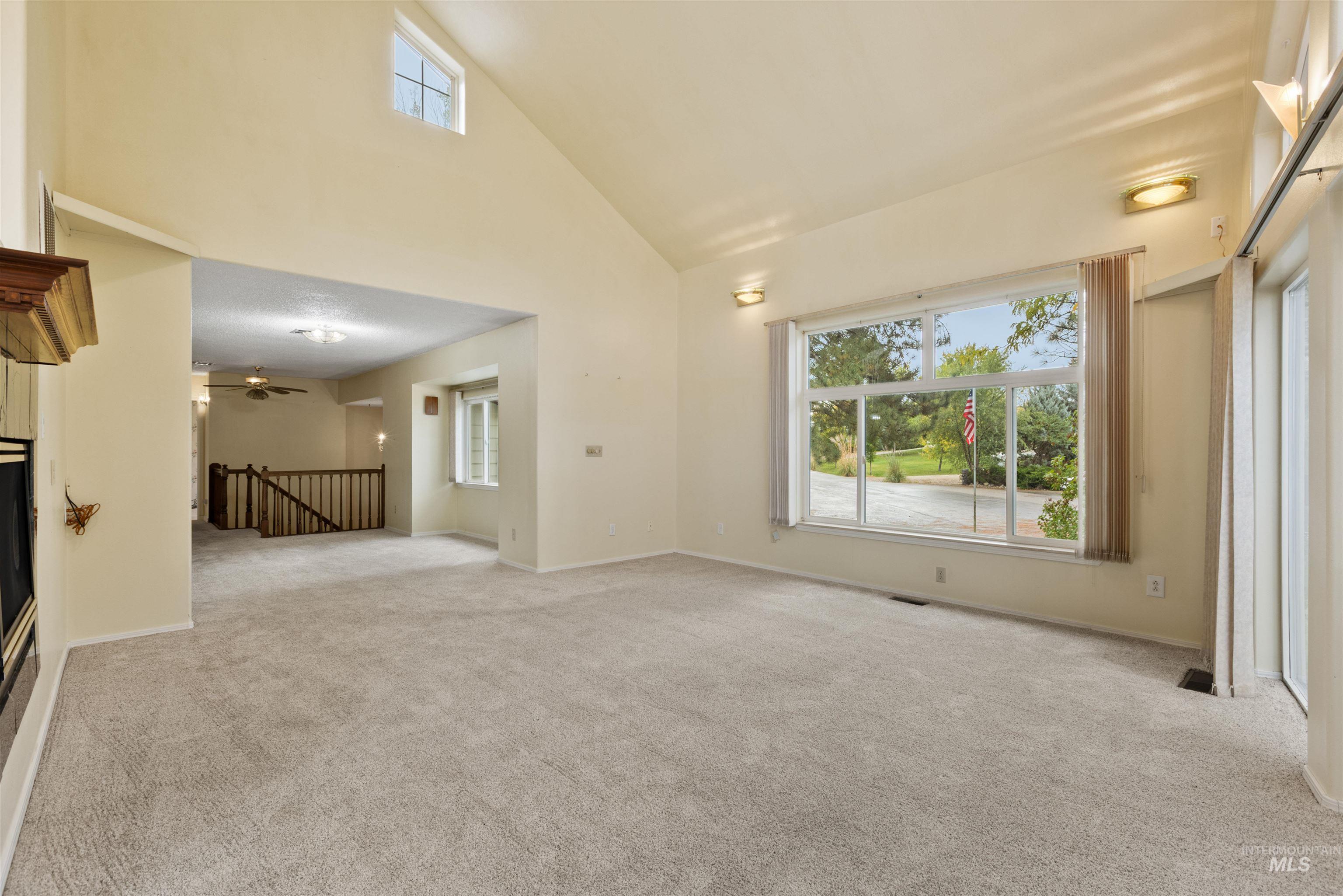 Unfurnished living room with high vaulted ceiling, light carpet, ceiling fan, and a glass covered fireplace