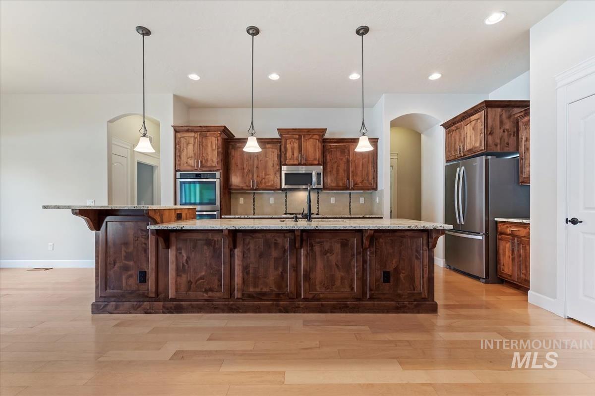 Kitchen featuring arched walkways, pendant lighting, a breakfast bar area, a large island with sink, and stainless steel appliances