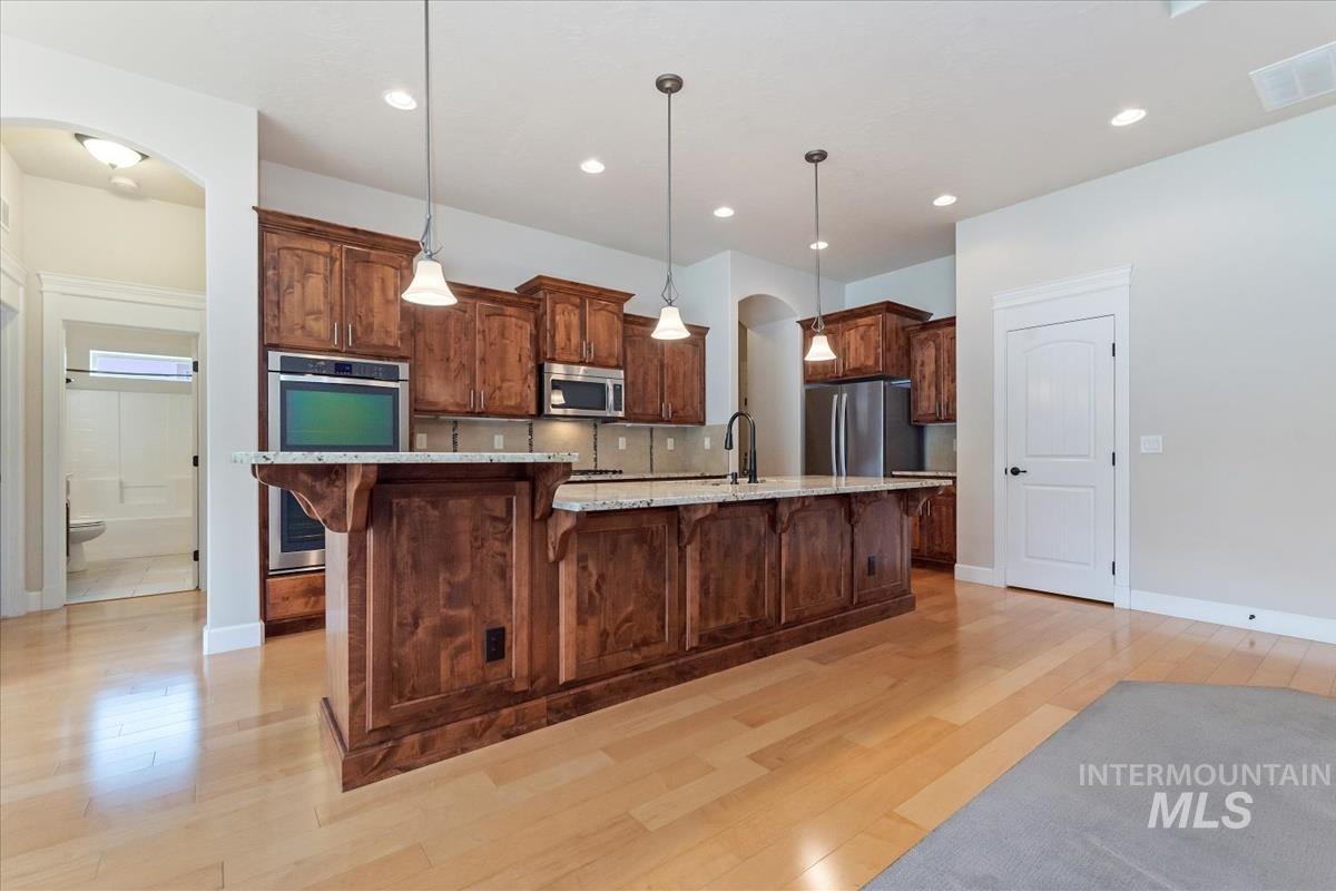 Kitchen featuring arched walkways, pendant lighting, a kitchen breakfast bar, light wood finished floors, and stainless steel appliances