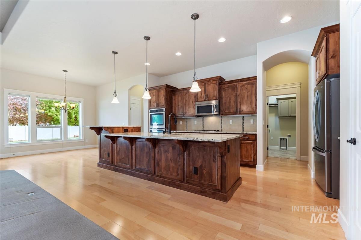 Kitchen with arched walkways, decorative light fixtures, appliances with stainless steel finishes, a breakfast bar, and light wood finished floors
