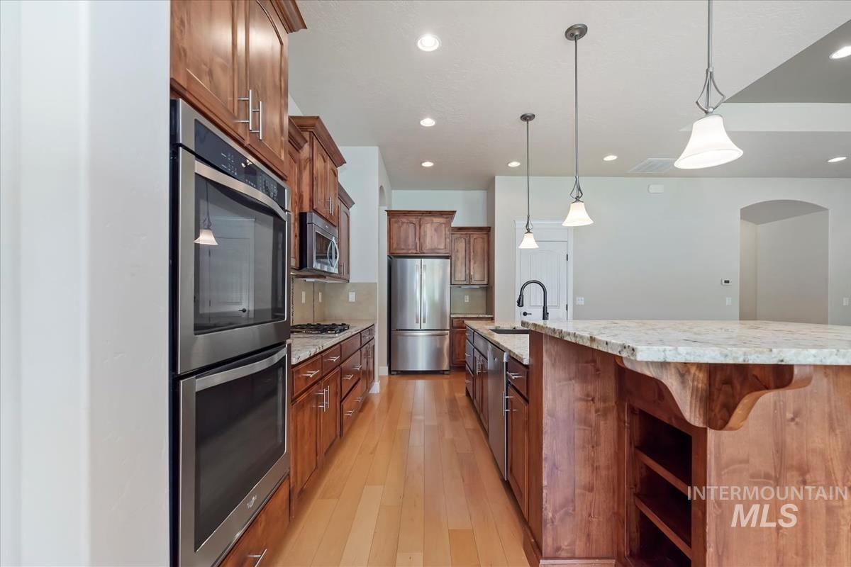 Kitchen with stainless steel appliances, light stone countertops, light wood-style floors, hanging light fixtures, and a large island with sink
