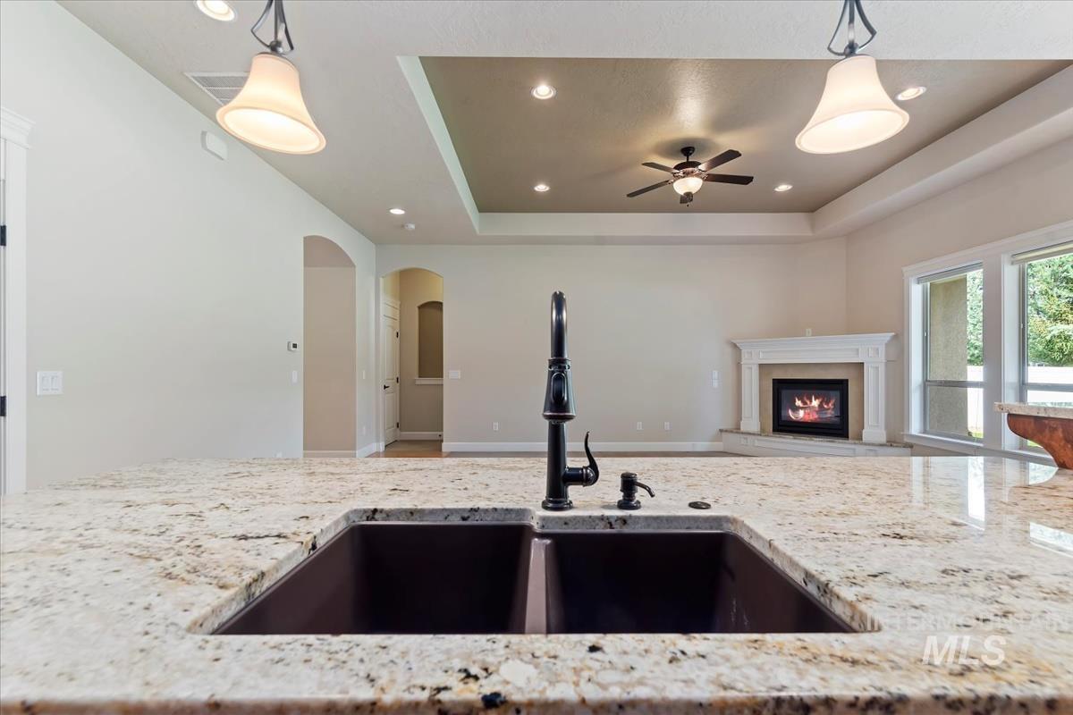 Kitchen with decorative light fixtures, a tray ceiling, recessed lighting, open floor plan, and light stone counters
