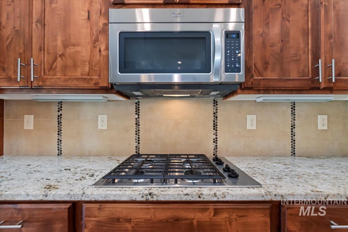 Kitchen view of light stone counters, appliances with stainless steel finishes, brown cabinetry, and tasteful backsplash