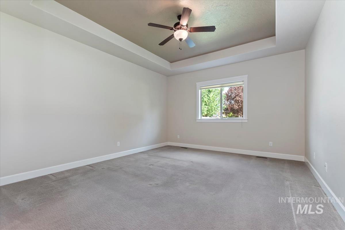 Unfurnished room featuring a tray ceiling, light carpet, and a ceiling fan