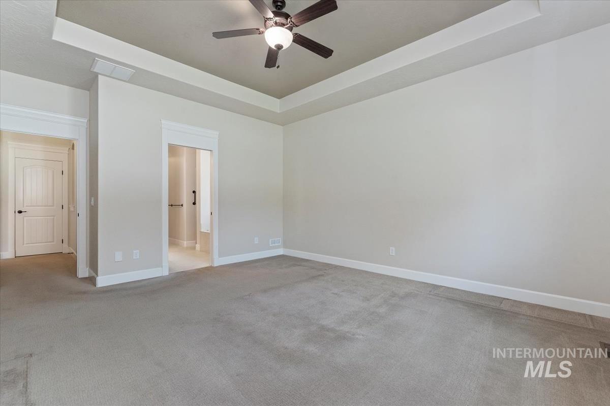 Unfurnished bedroom with a raised ceiling, light colored carpet, and a ceiling fan