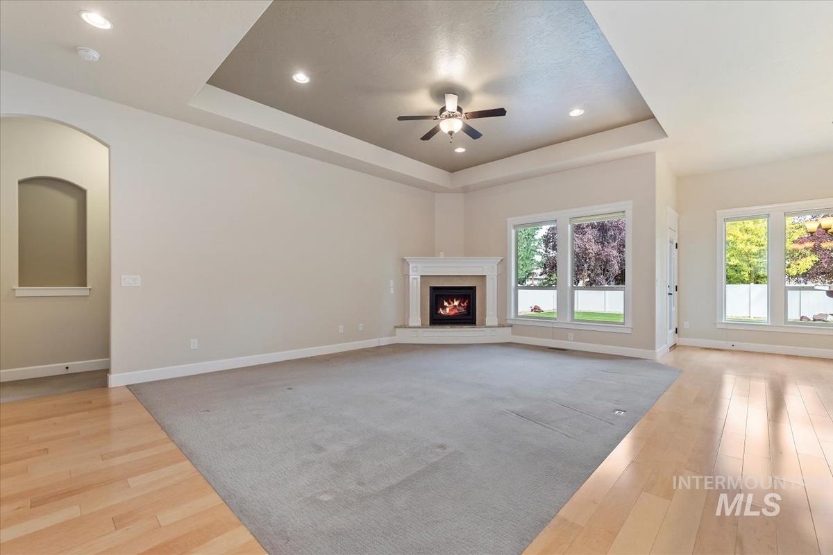 Unfurnished living room with a tray ceiling, light wood-style flooring, recessed lighting, ceiling fan, and a lit fireplace