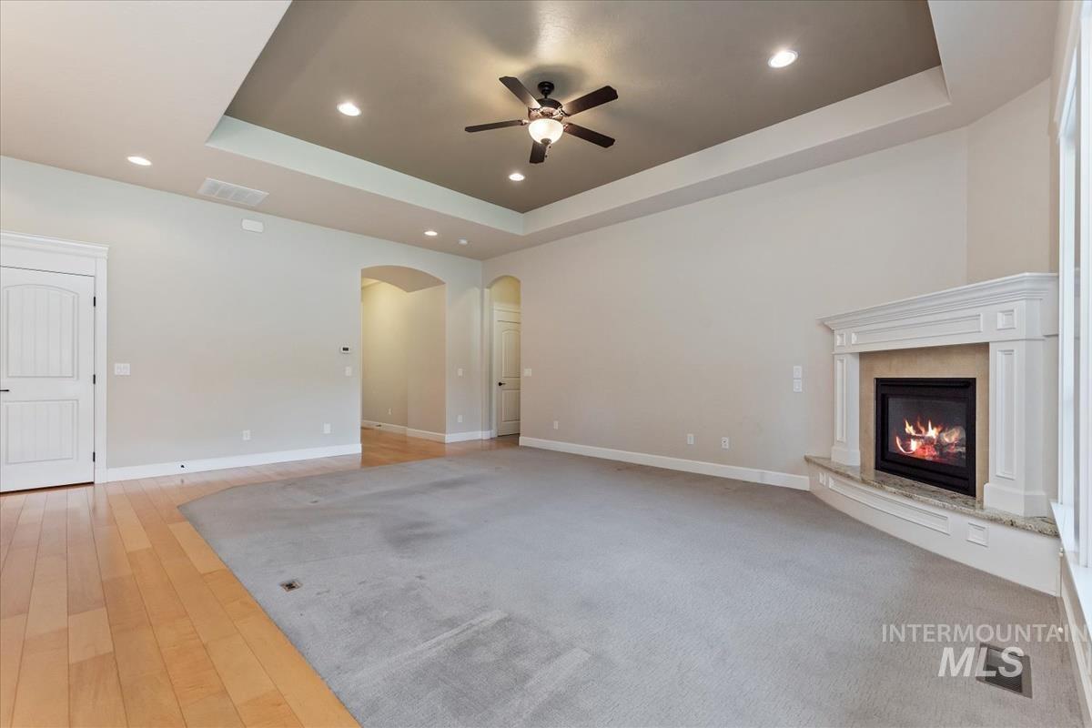 Unfurnished living room with a raised ceiling, a glass covered fireplace, recessed lighting, light wood finished floors, and ceiling fan