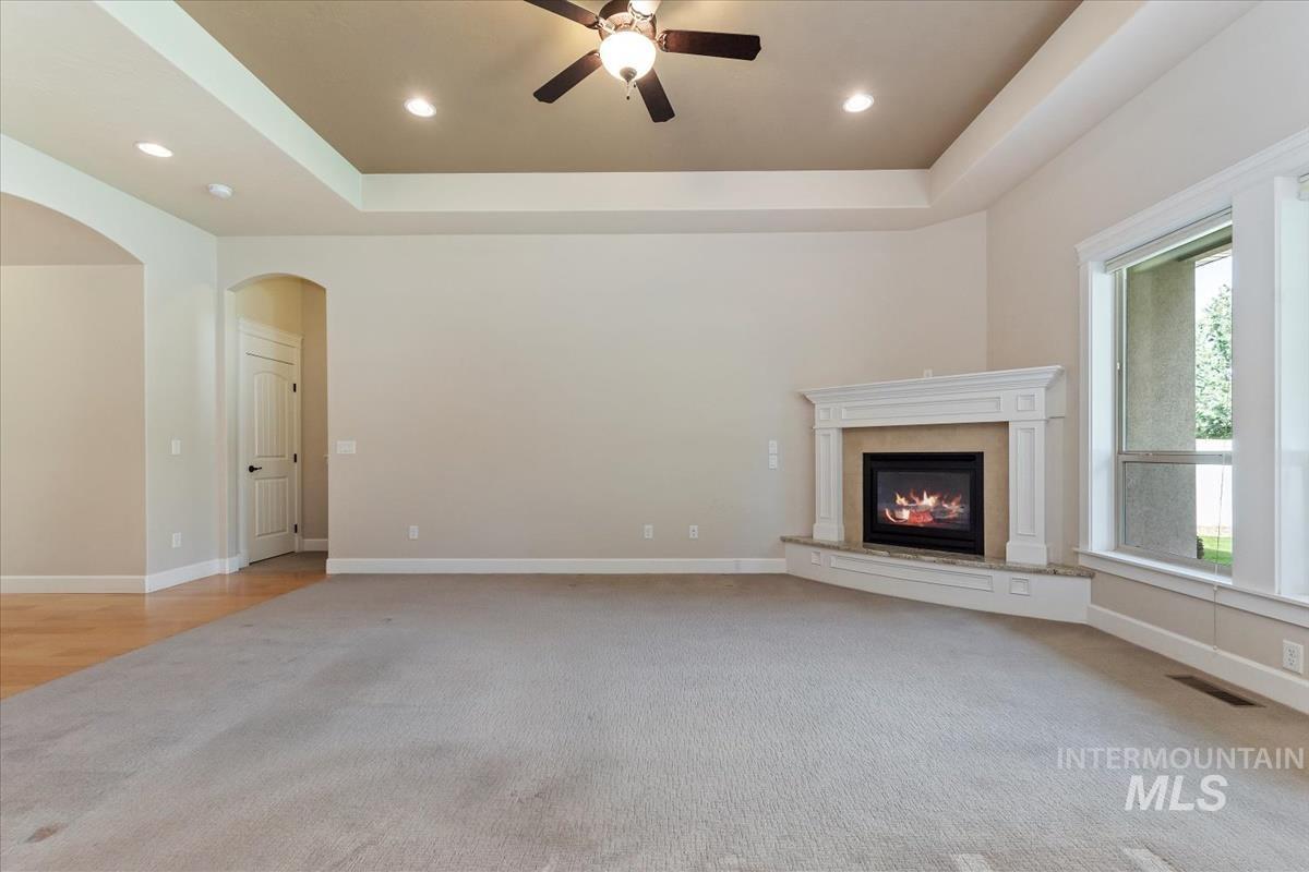 Unfurnished living room featuring a raised ceiling, light carpet, a high end fireplace, ceiling fan, and recessed lighting