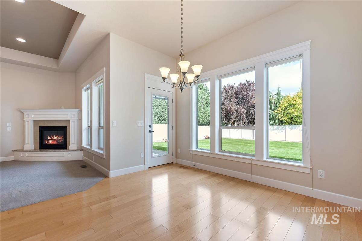 Unfurnished dining area with light wood-style flooring, a fireplace, a chandelier, a tray ceiling, and recessed lighting