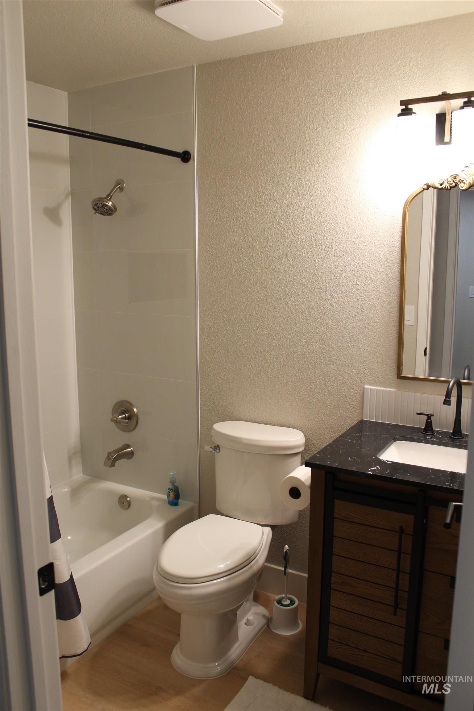 Full bath featuring a textured wall, vanity, wood finished floors, and shower / tub combo