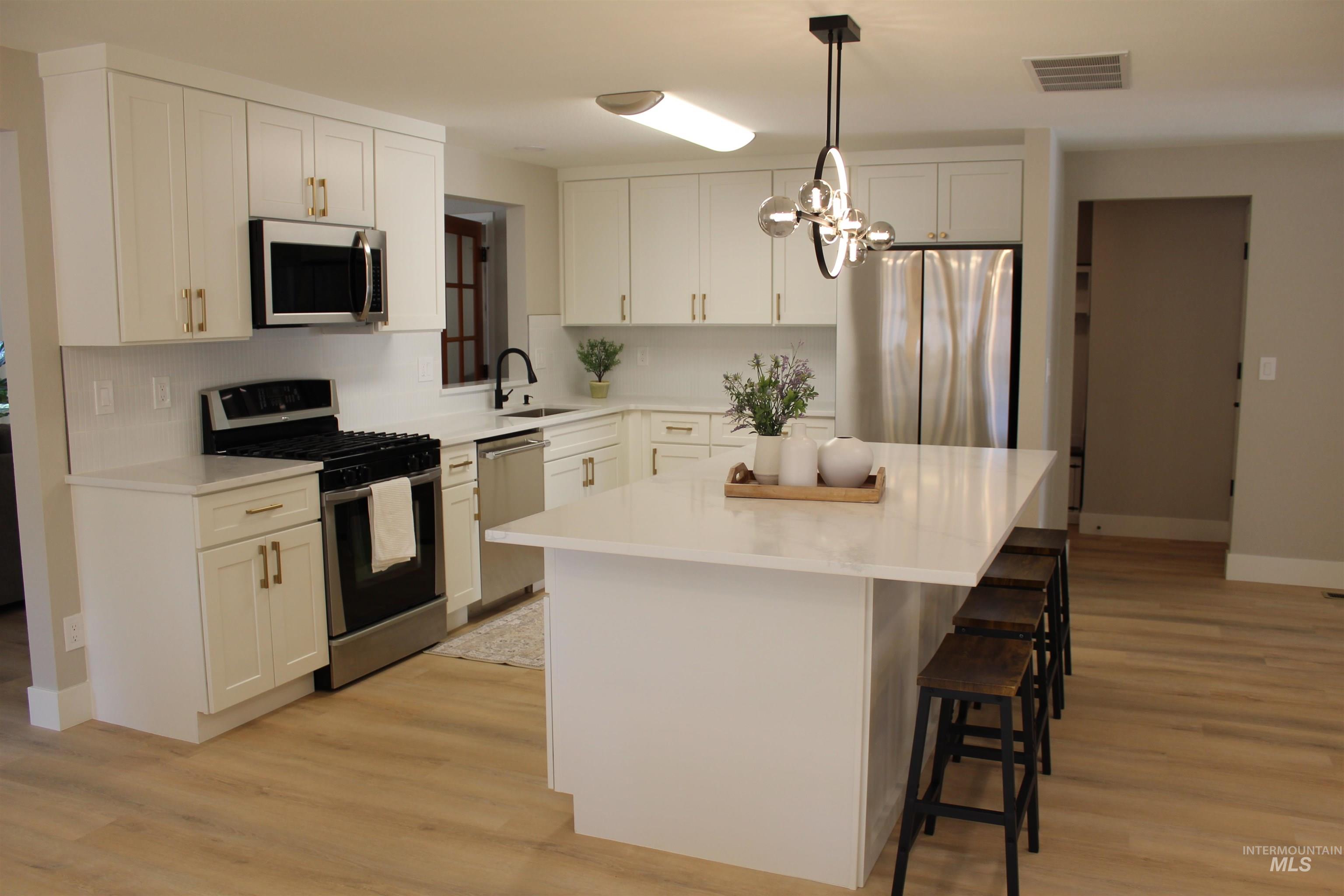 Kitchen featuring stainless steel appliances, a kitchen island, a kitchen breakfast bar, and light wood-style floors