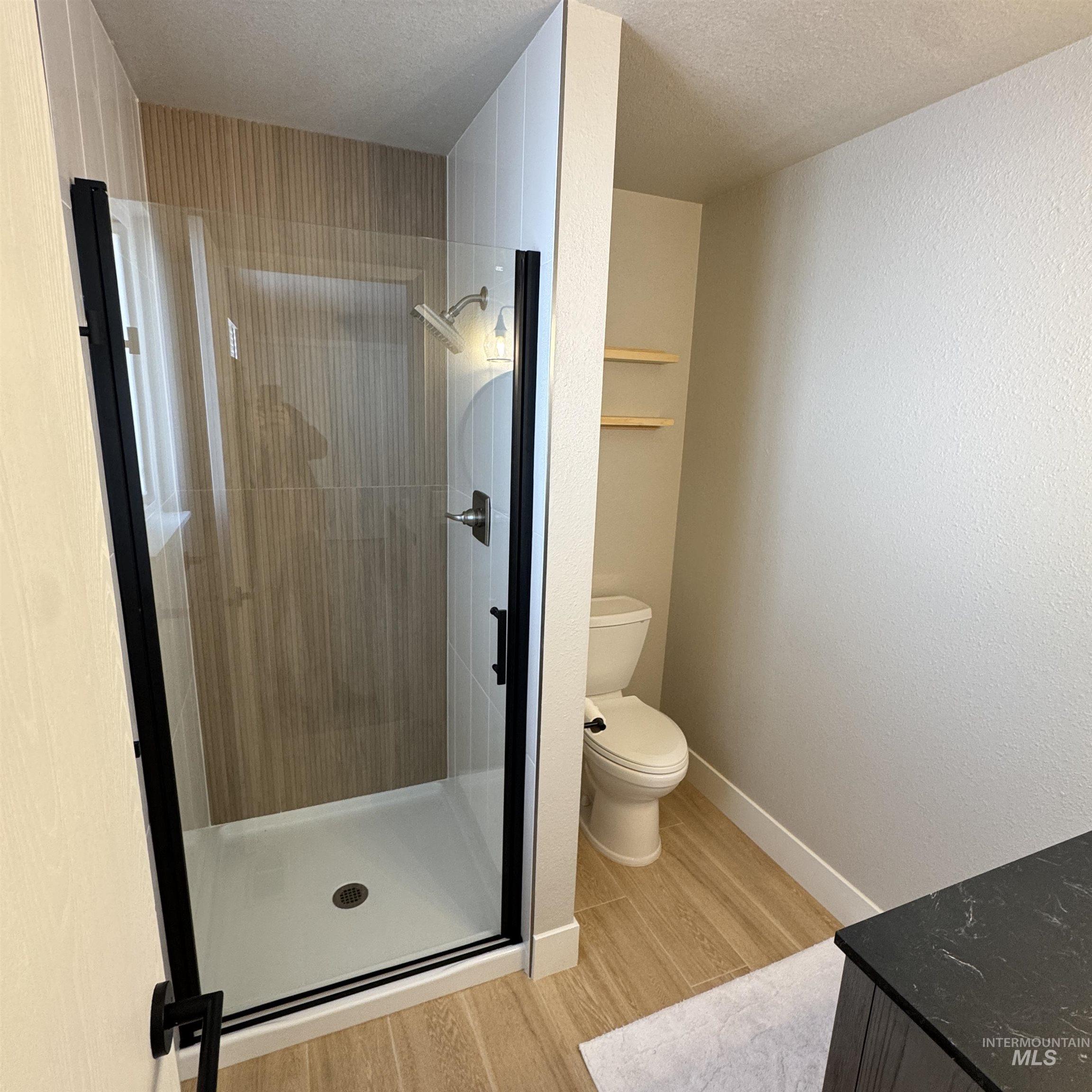 Full bath featuring light wood-type flooring, vanity, a stall shower, and a textured ceiling