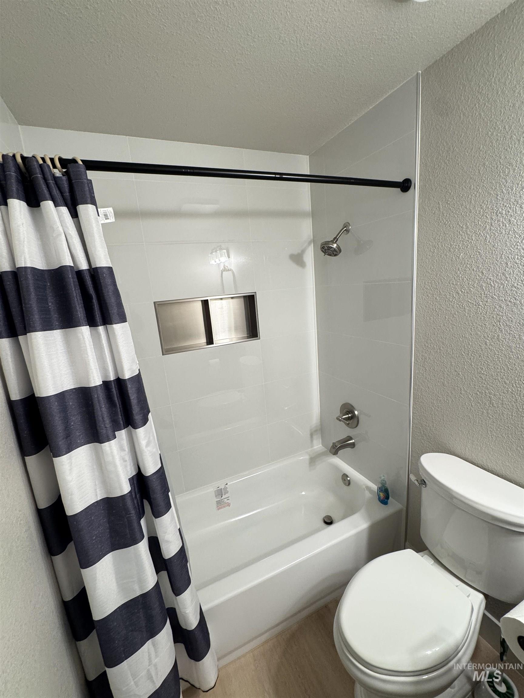 Full bathroom with a textured wall, a textured ceiling, shower / tub combo, and wood finished floors