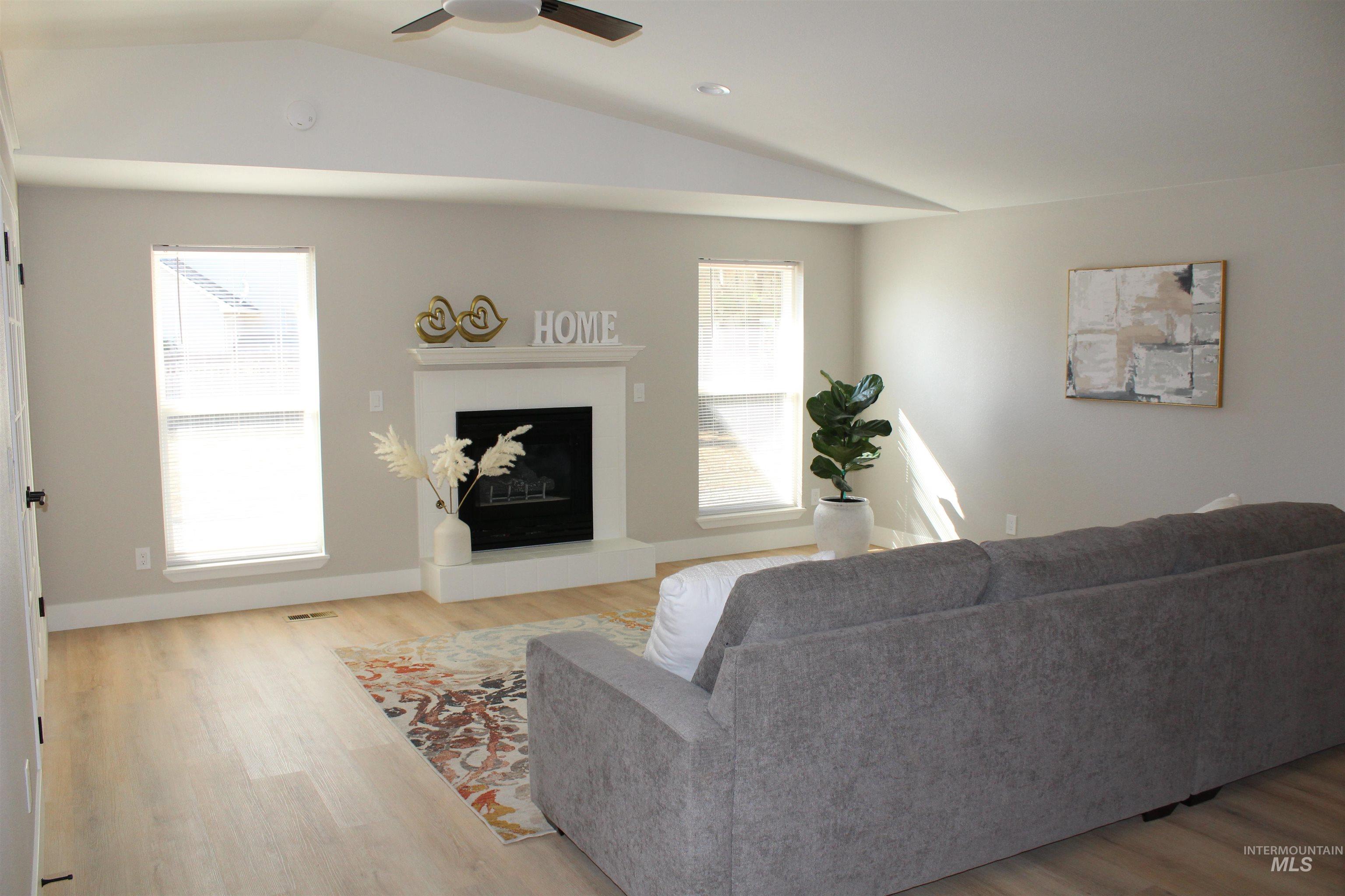 Living room with a fireplace with raised hearth, light wood-style flooring, vaulted ceiling, and a ceiling fan