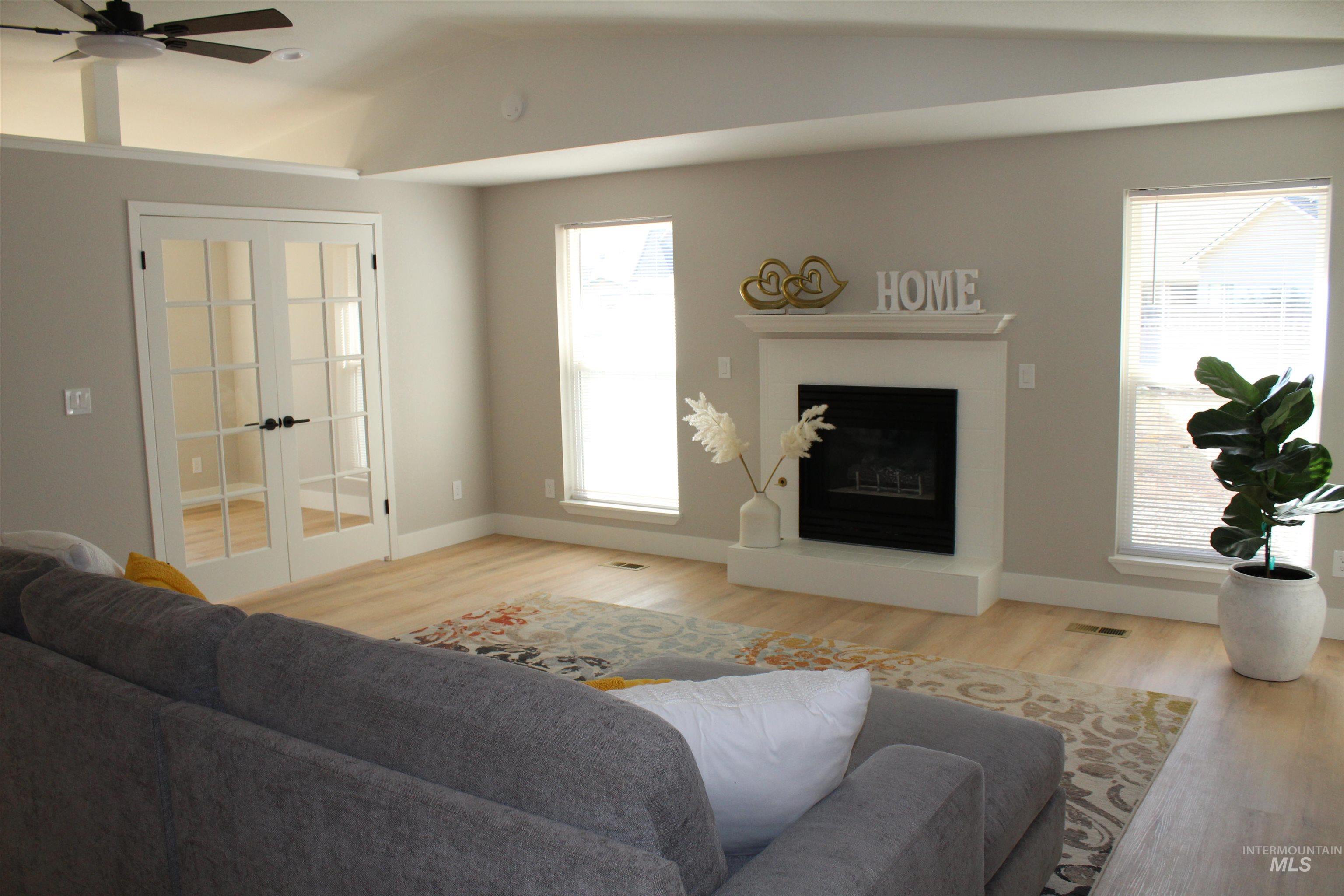 Living room featuring wood finished floors, a fireplace with raised hearth, lofted ceiling, a ceiling fan, and french doors