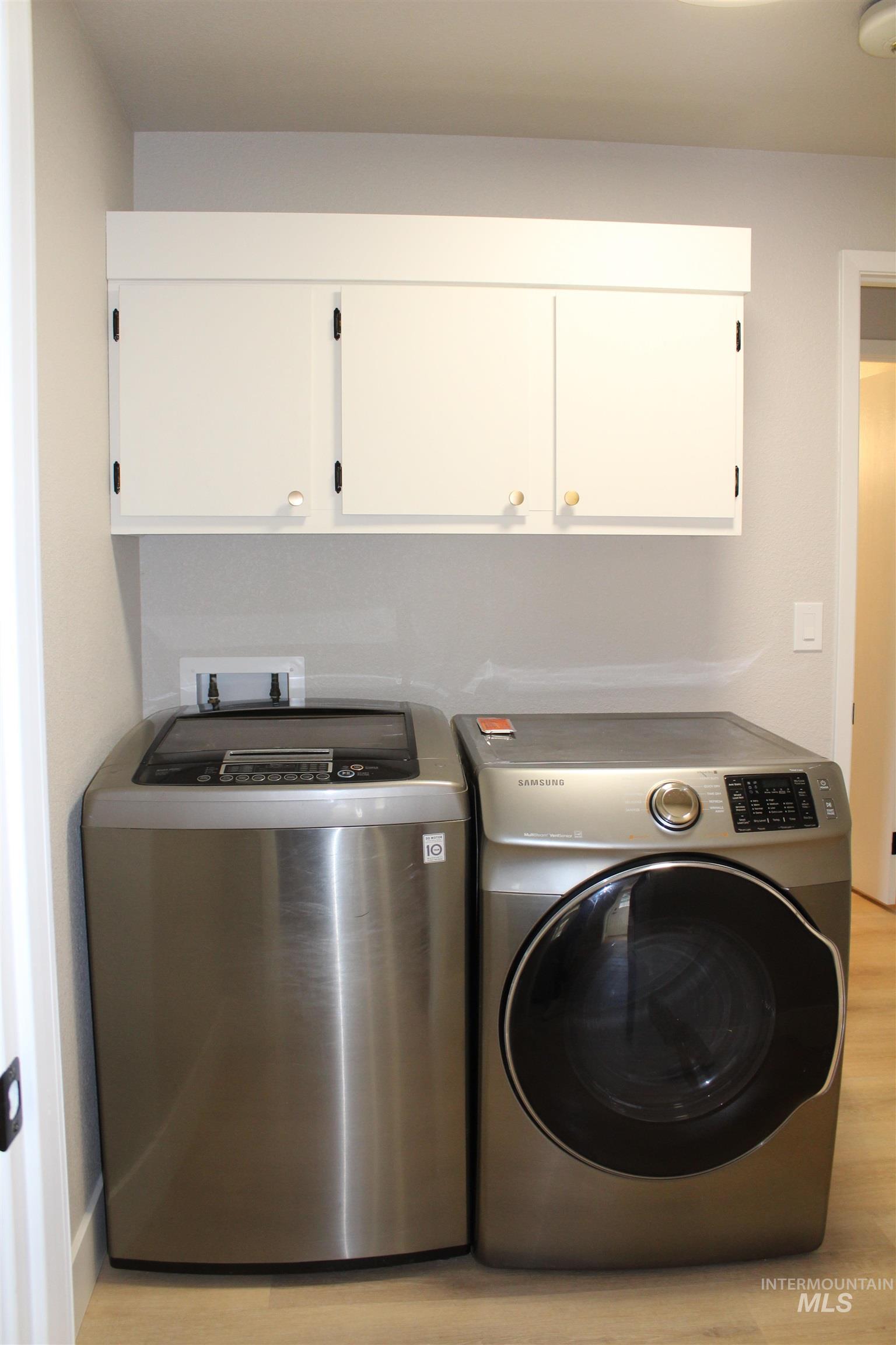 Laundry area with light wood-type flooring, washer and dryer, and cabinet space