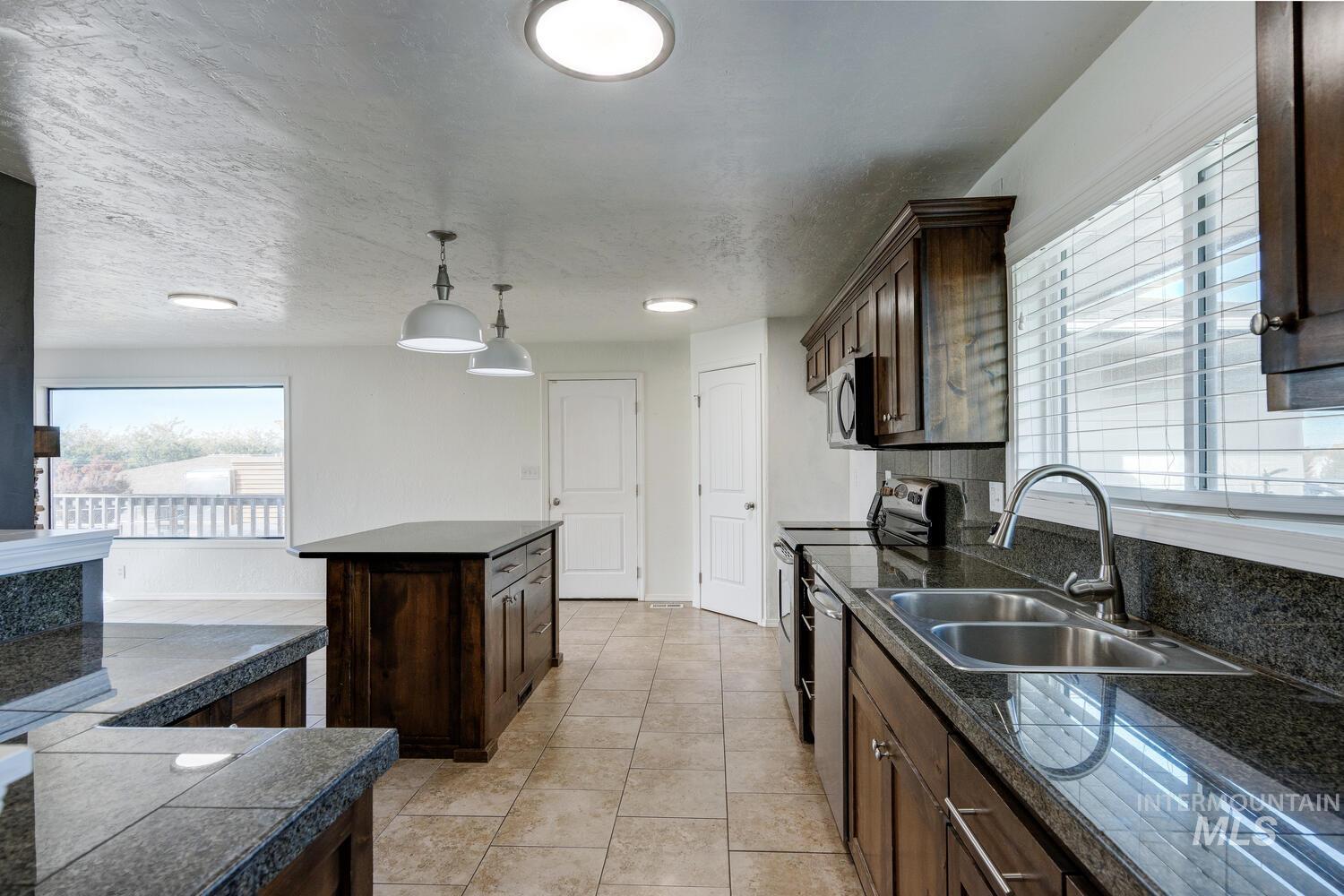 Kitchen featuring tile counters, stainless steel appliances, decorative light fixtures, a kitchen island, and dark brown cabinets